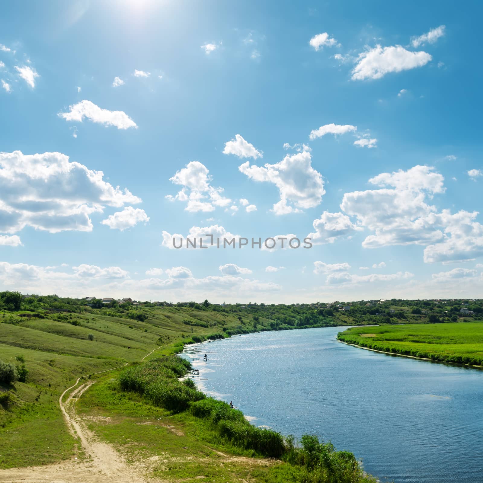 sun in blue sky with clouds over river