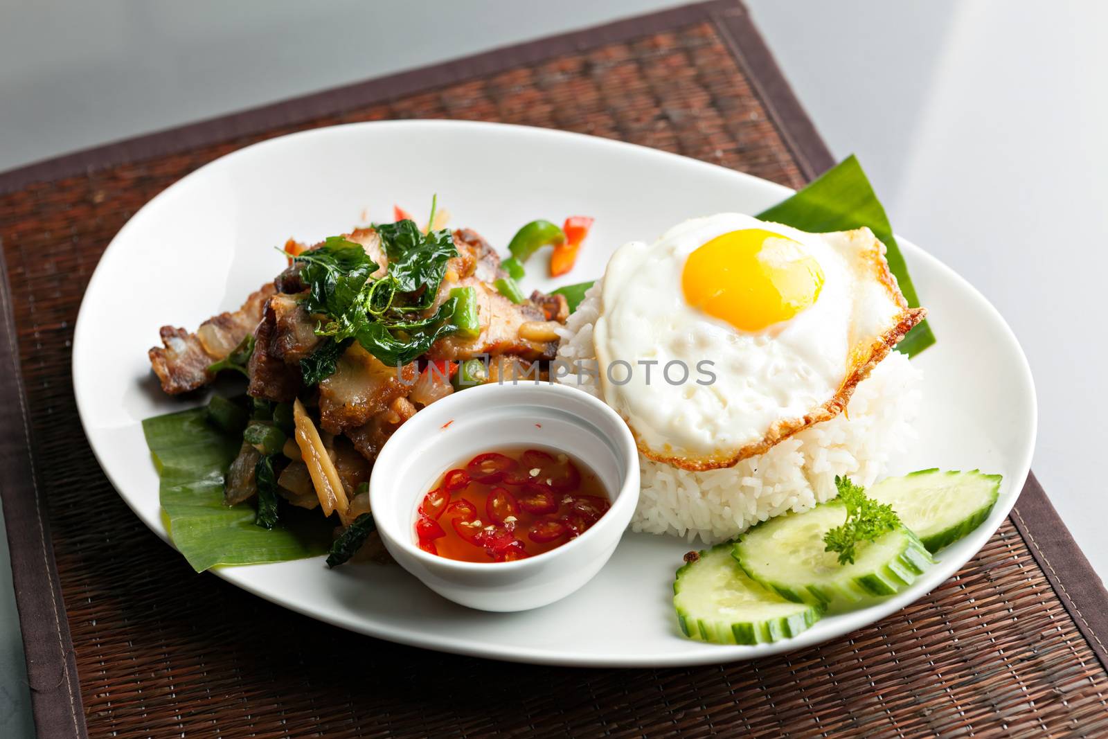 Traditional Thai dish crispy pork with a fried egg atop the jasmine rice served with chili sauce.