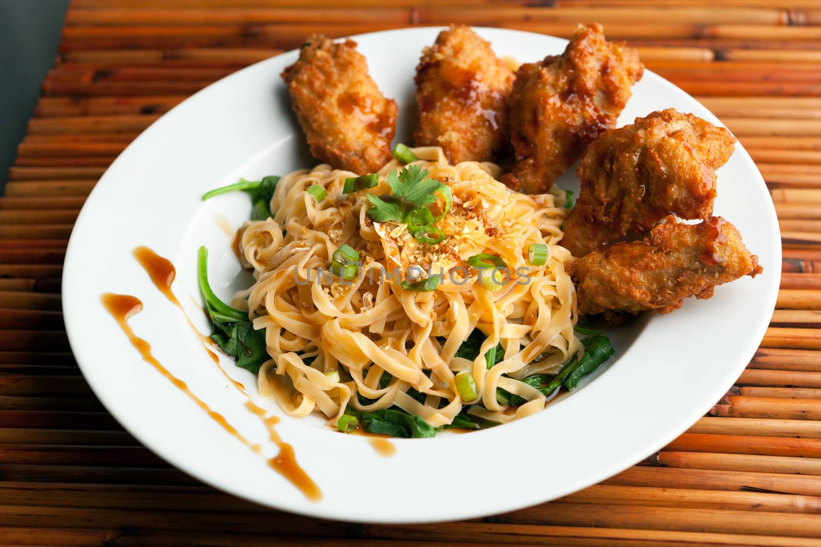 Thai style fried chicken wings on a round white plate with egg noodles and spinach.
