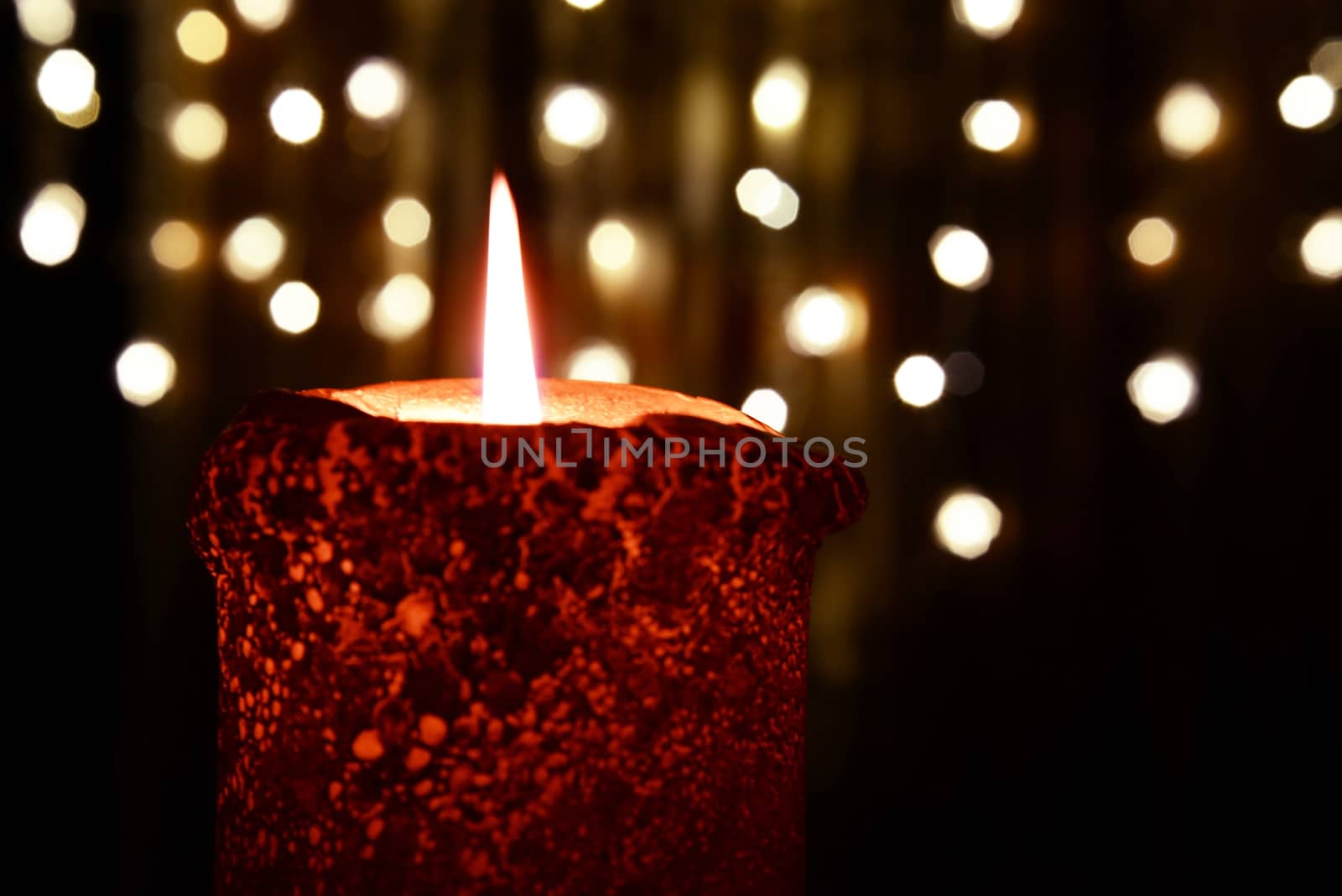 Photo of an orange candle burning over Christmas lights background.