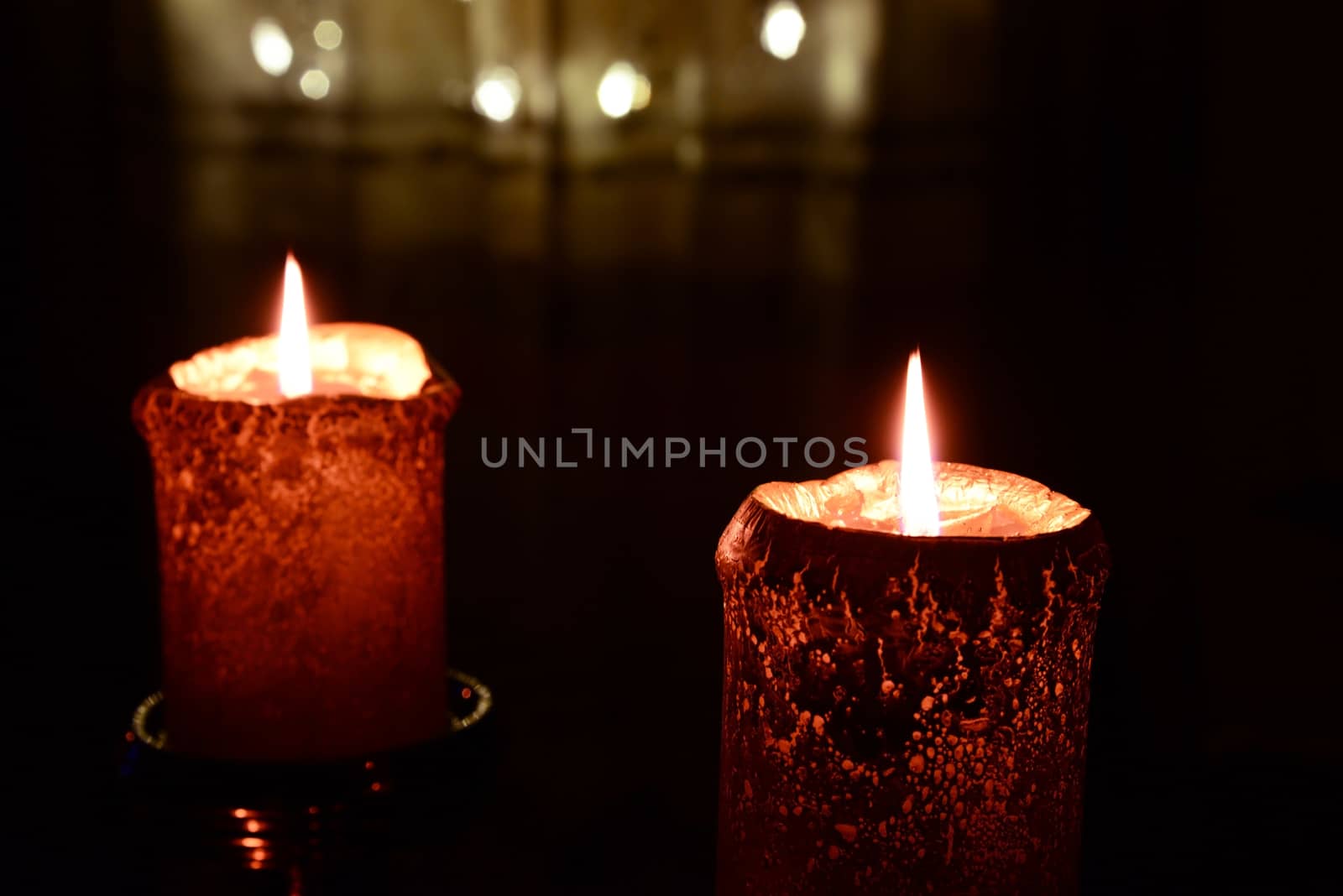 Photo of two orange candles burning over Christmas lights background.