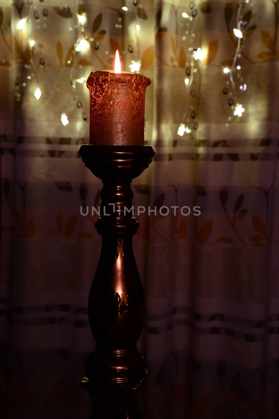 Photo of an orange candle burning over Christmas lights background.