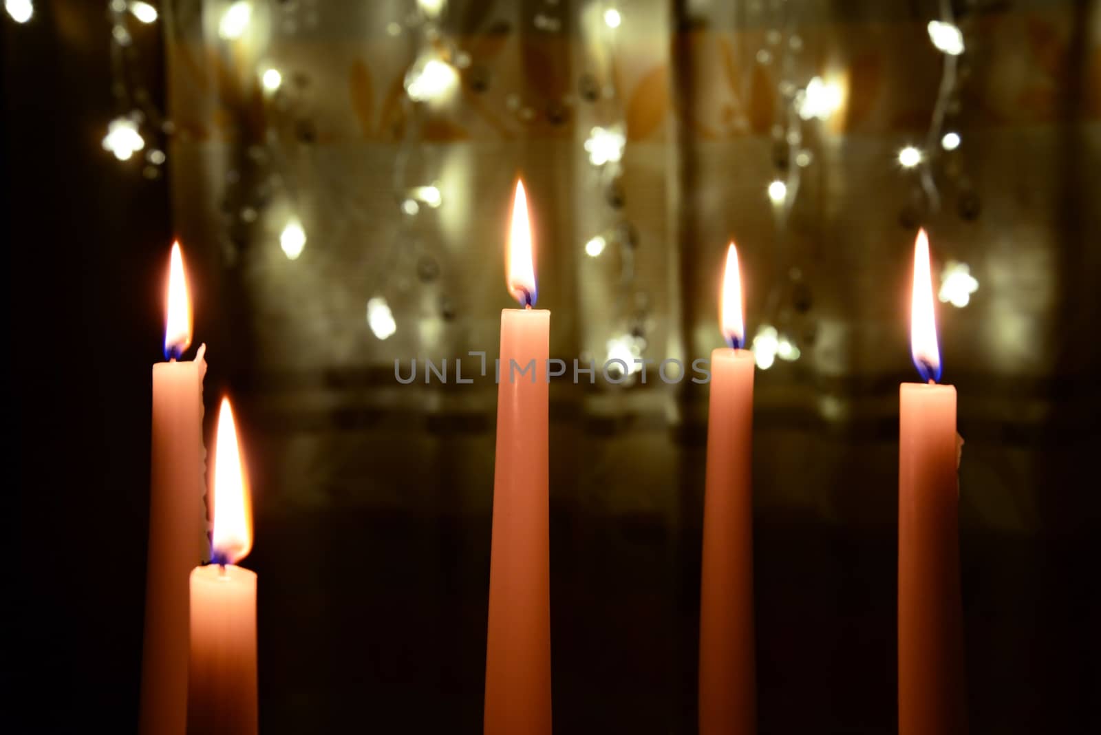 Photo of five white candles burning over Christmas lights background.