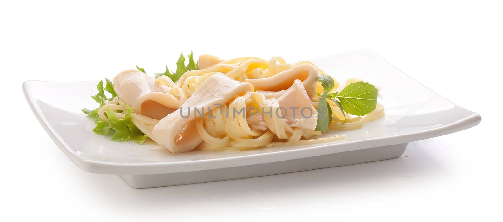 Some squid rings with pasta, fresh green lettuce and basil on the white plate