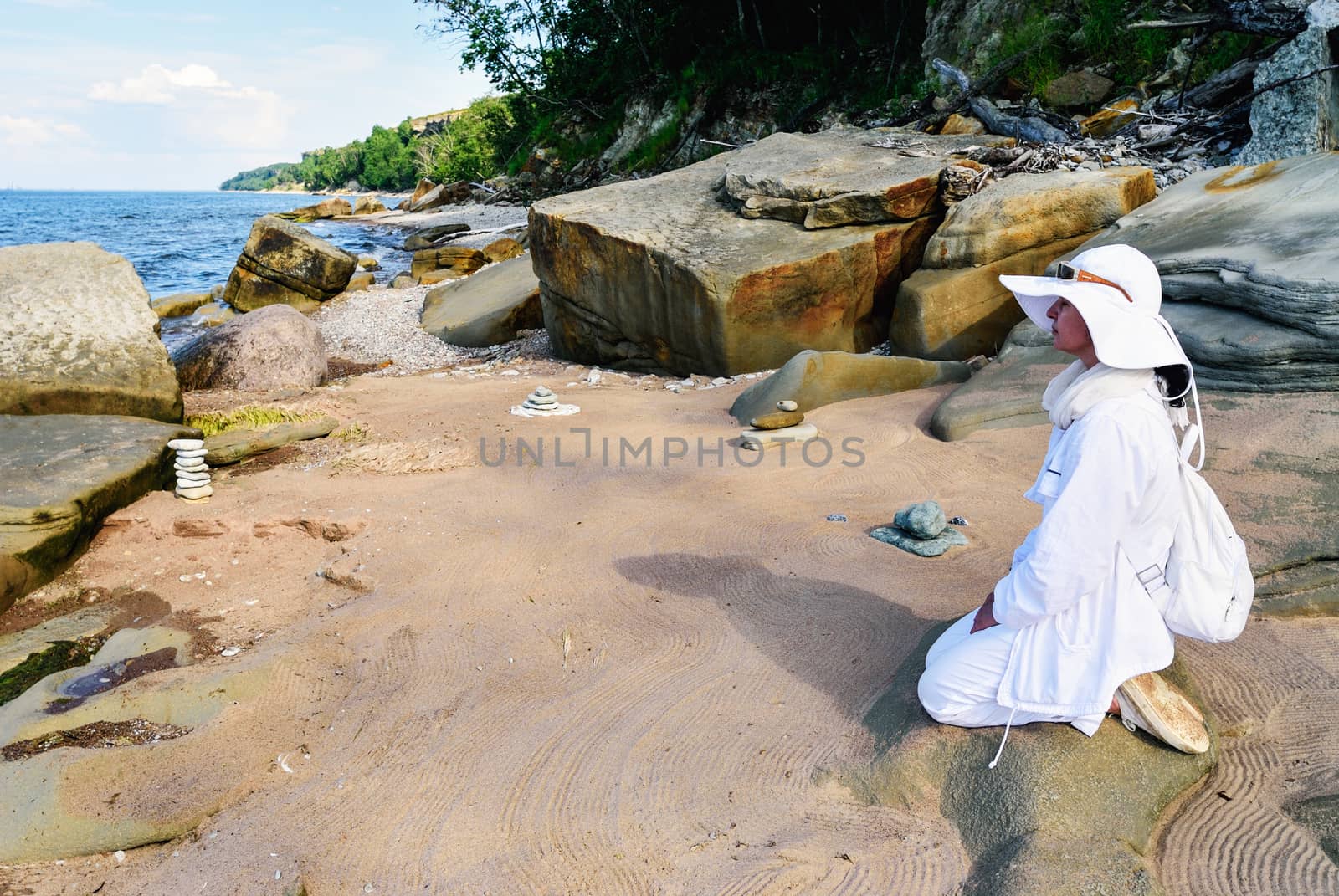 Woman in white meditates between sea stones on the coast