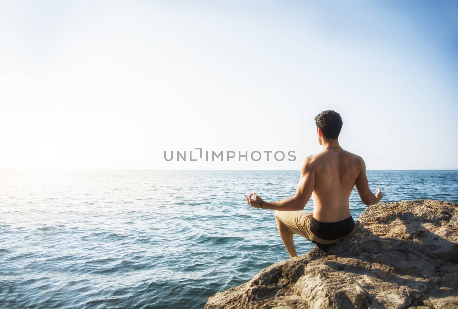 Young Man Meditating or Doing Yoga Exercise by Sea by artofphoto