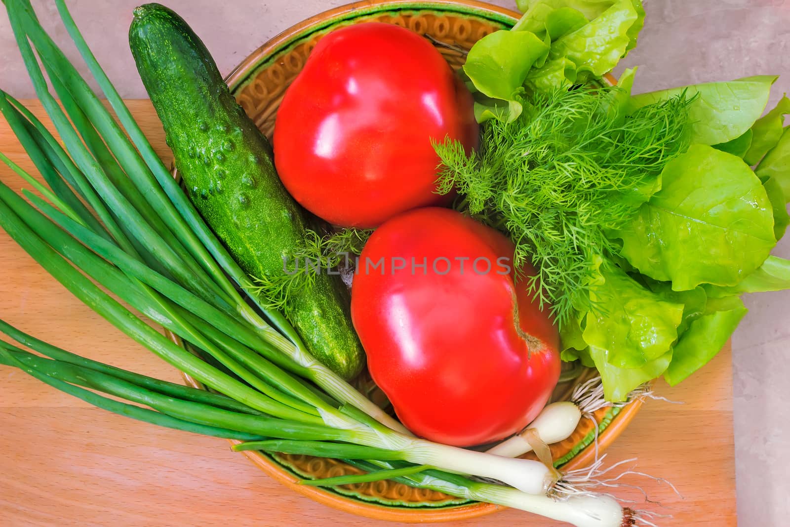 On a ceramic dish are large ripe tomatoes, cucumber, green onions, lettuce. Presents closeup.