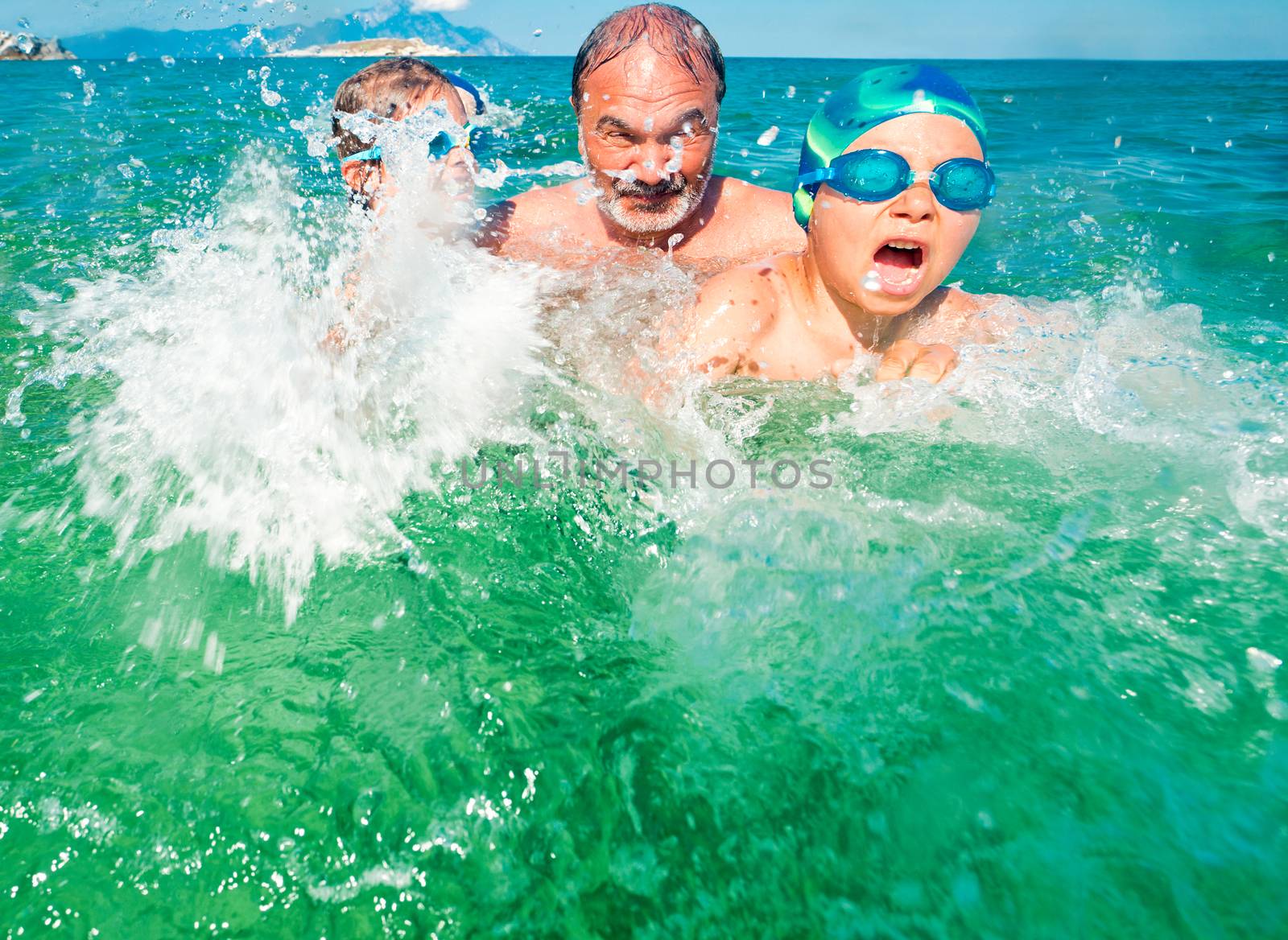 Grandfather with his grandson and granddauther playing in the sea, splashing water all arround.