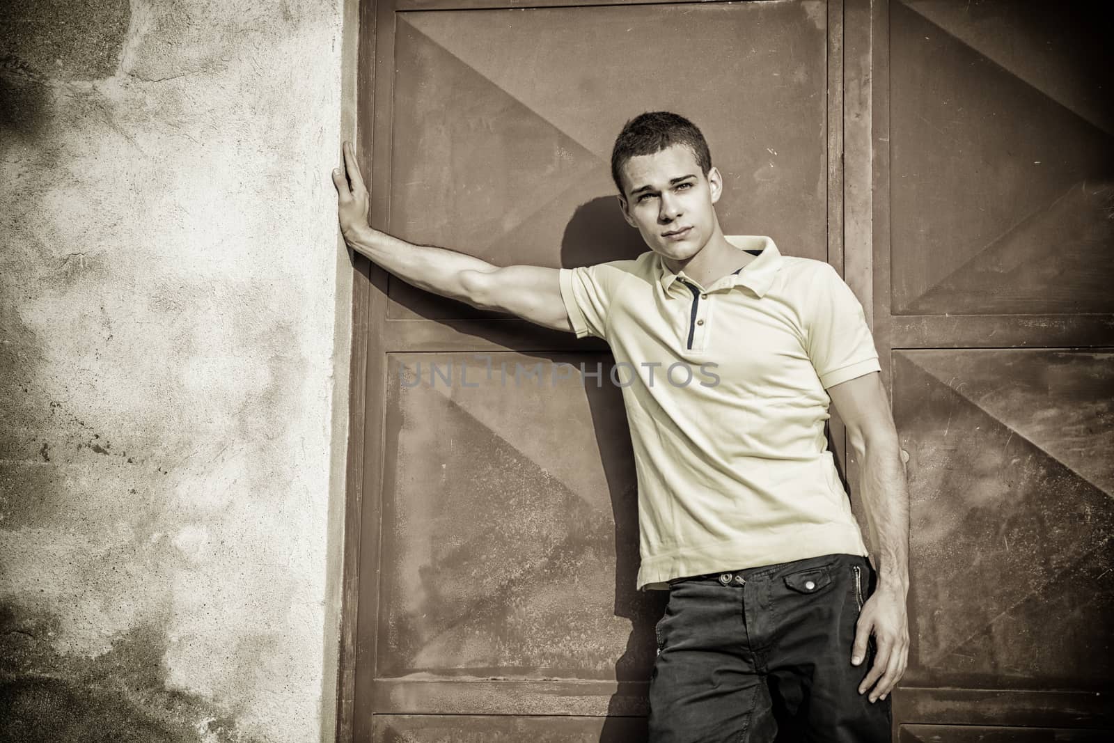 Attractive green eyed young man leaning against rough concrete wall, looking at camera