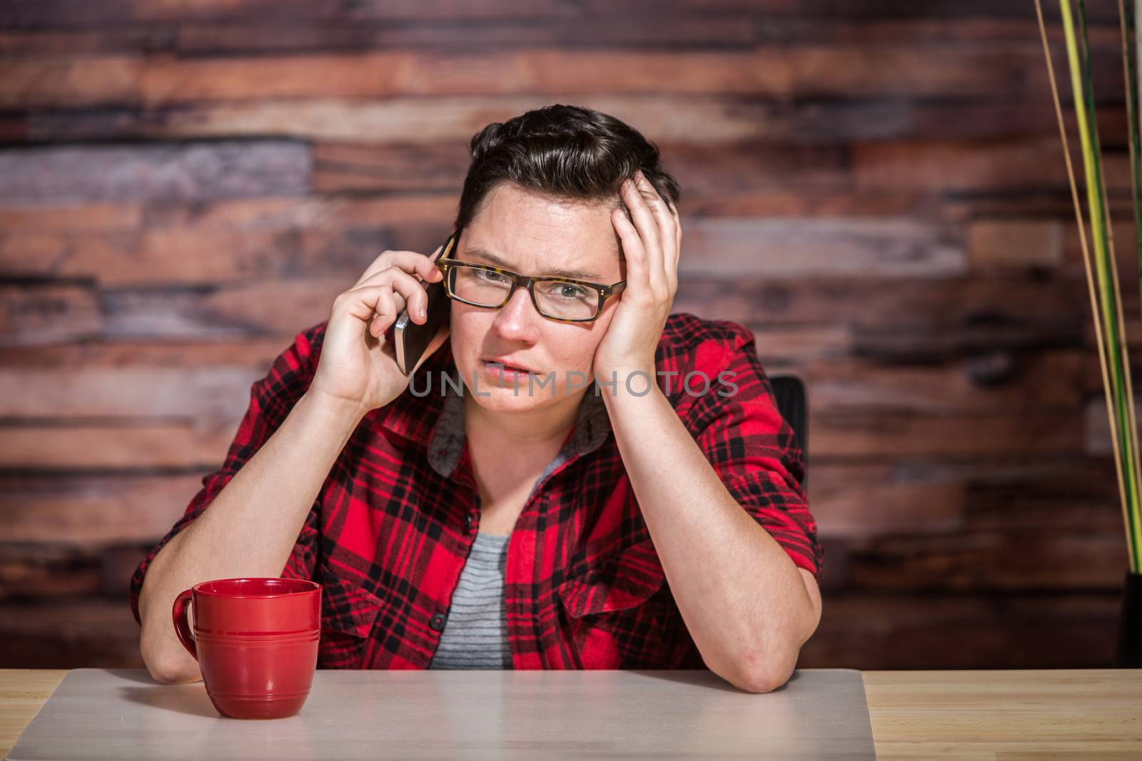 Serious woman wearing flannel shirt on smart phone in office