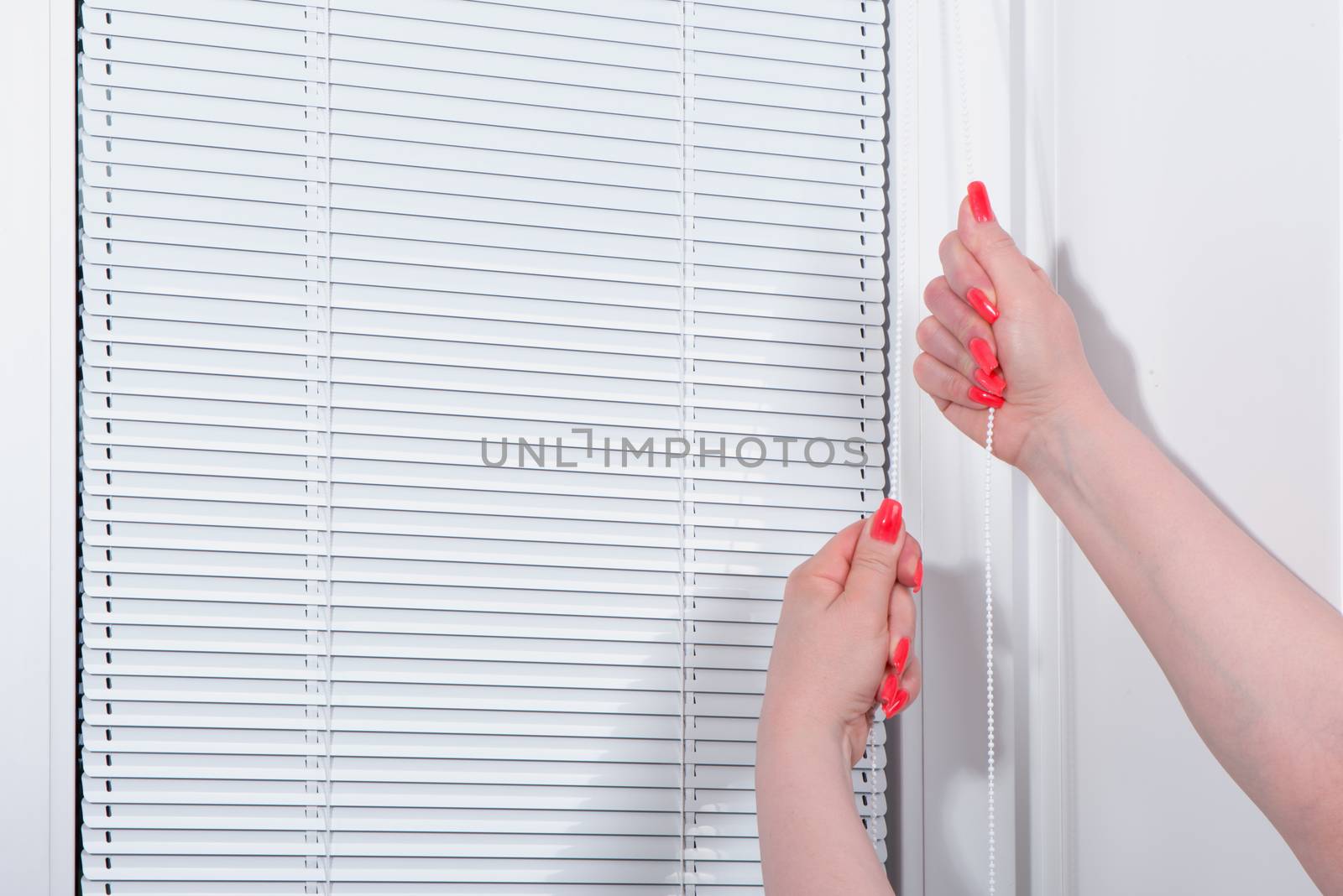 Female hands with manicure close white blinds at window