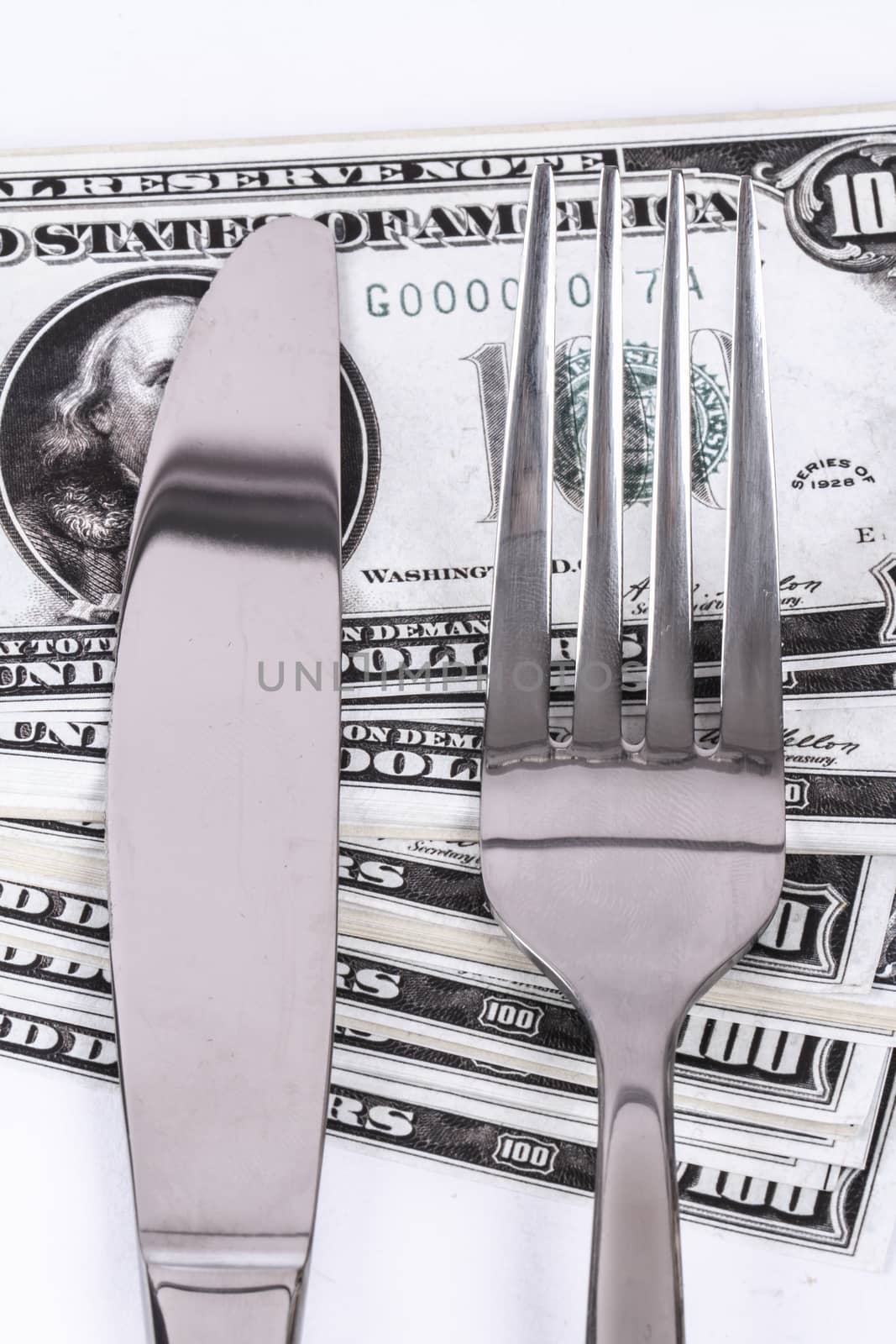Close up detailed view of one hundred dollar banknotes under a steel fork and knife, isolated on white background.
