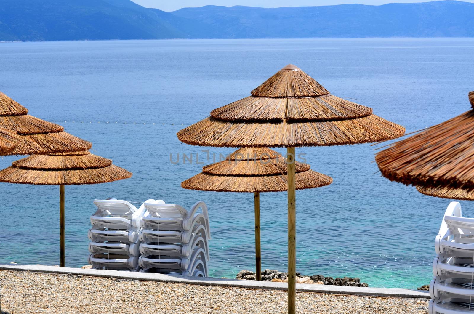 Umbrellas on a beach with clear water and blue slippers