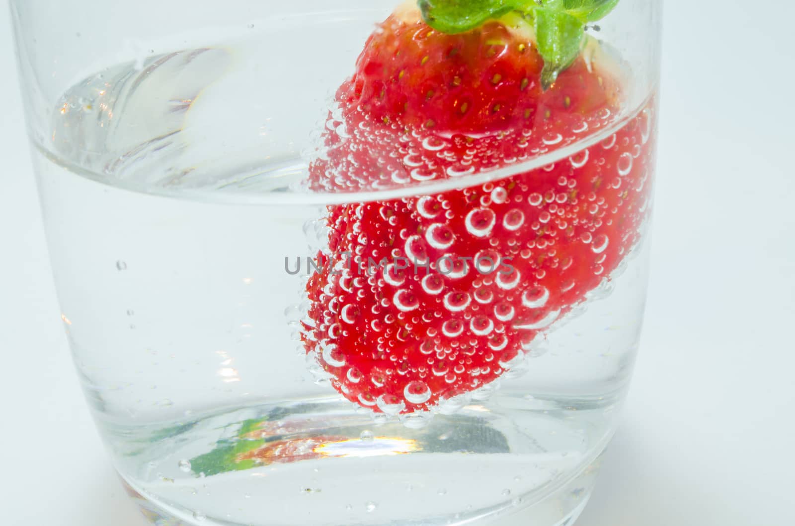 Close-up of strawberry floating in sparkling mineral water glass.