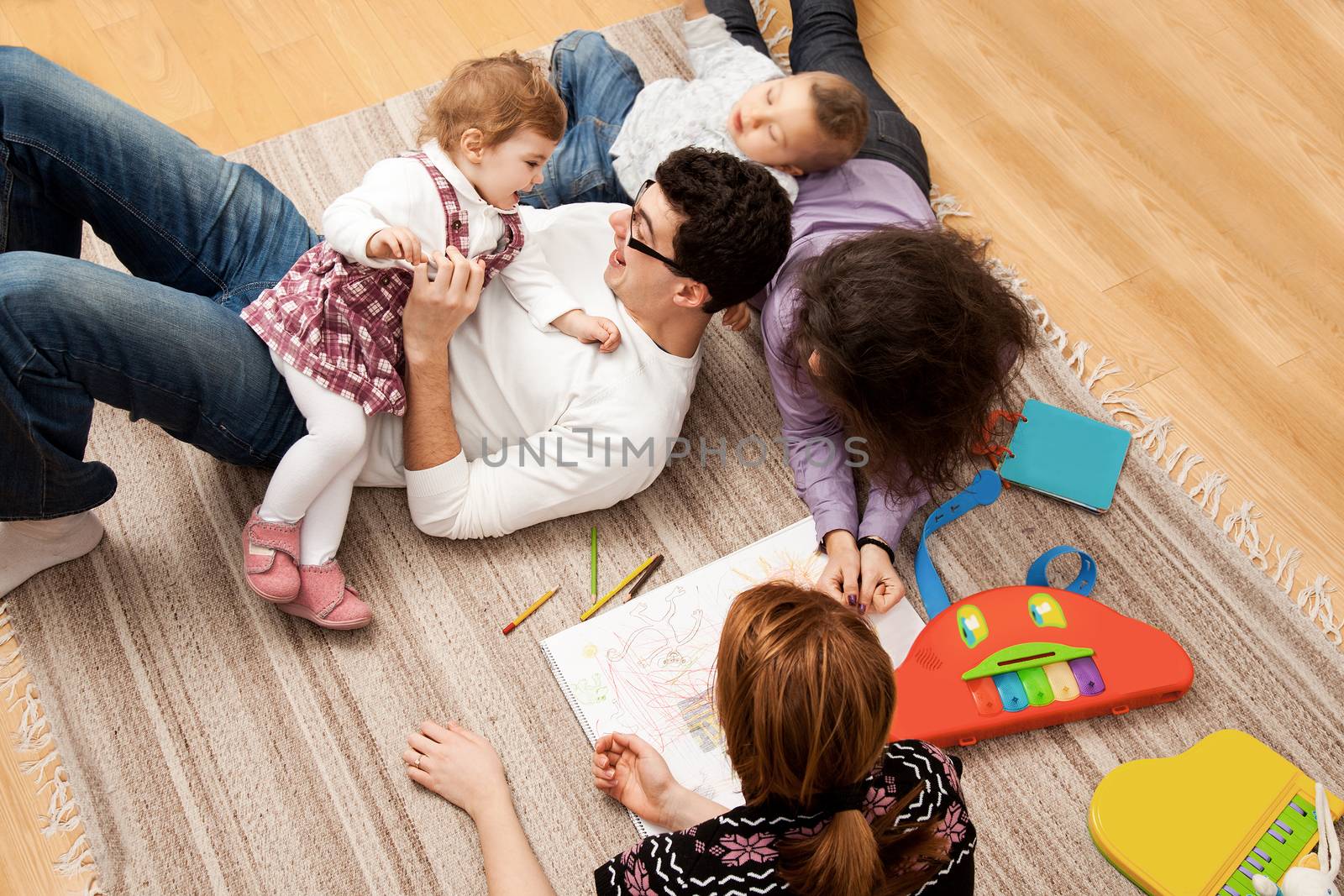 friends or relatives family group of five - two babies and three adults lying on the carpet, dad is tickling his daughter.