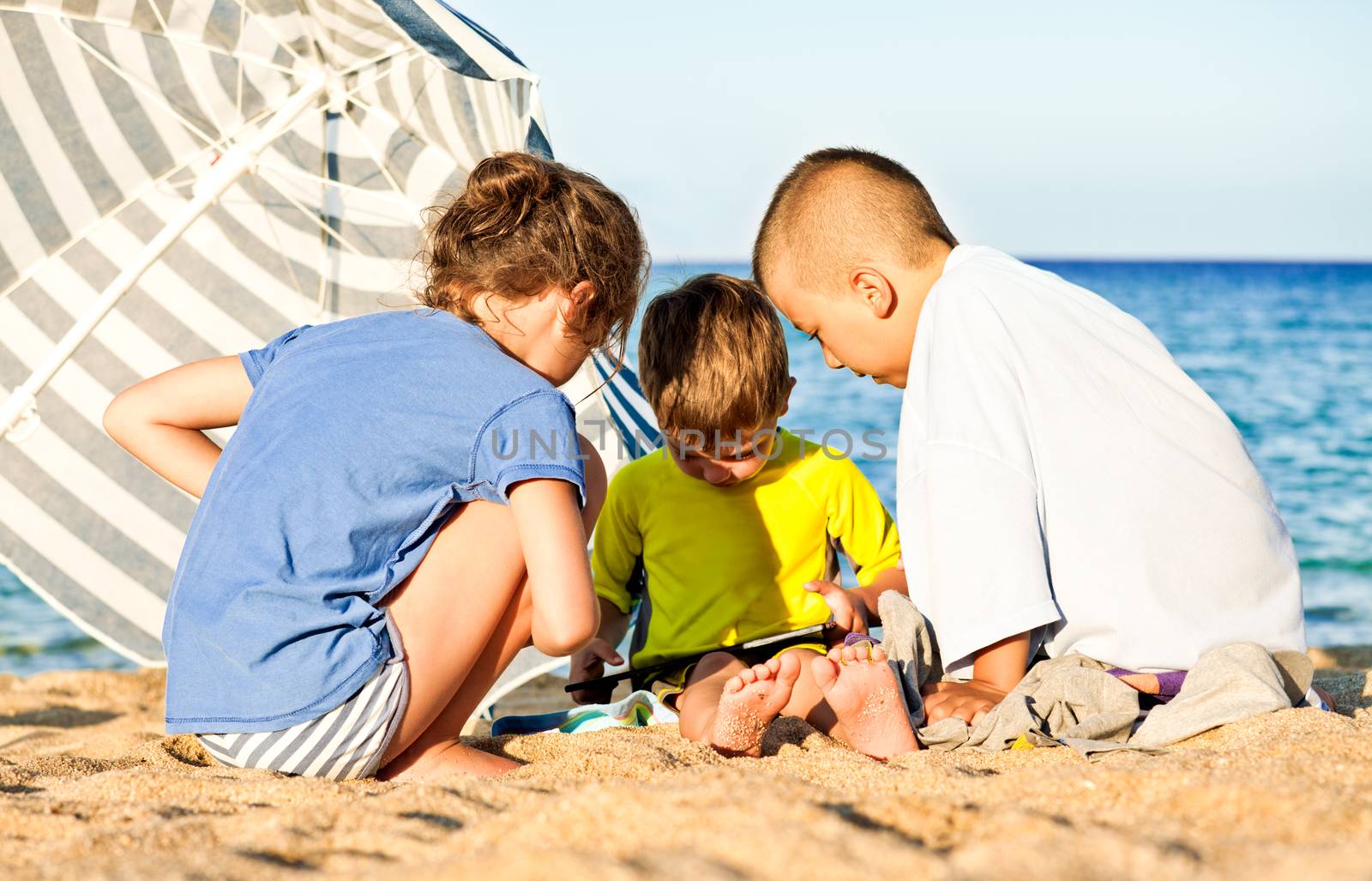 Tree children playing on a video game at the beach under the hot summer sun.