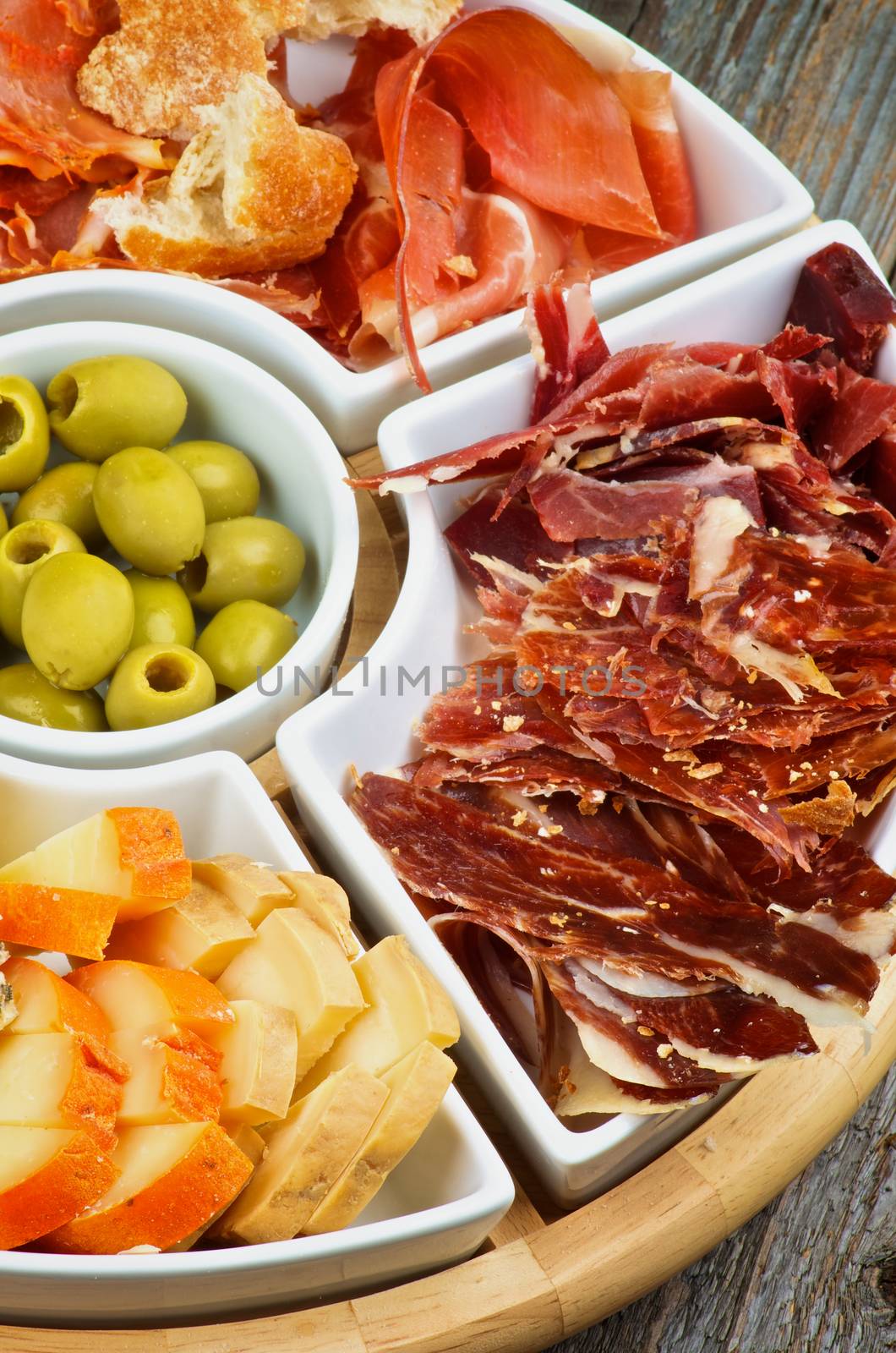 Arrangement of Spanish Snacks with Various Cheeses, Jamon, Cured Ham and Green Olives on Serving Plate closeup on Wooden background