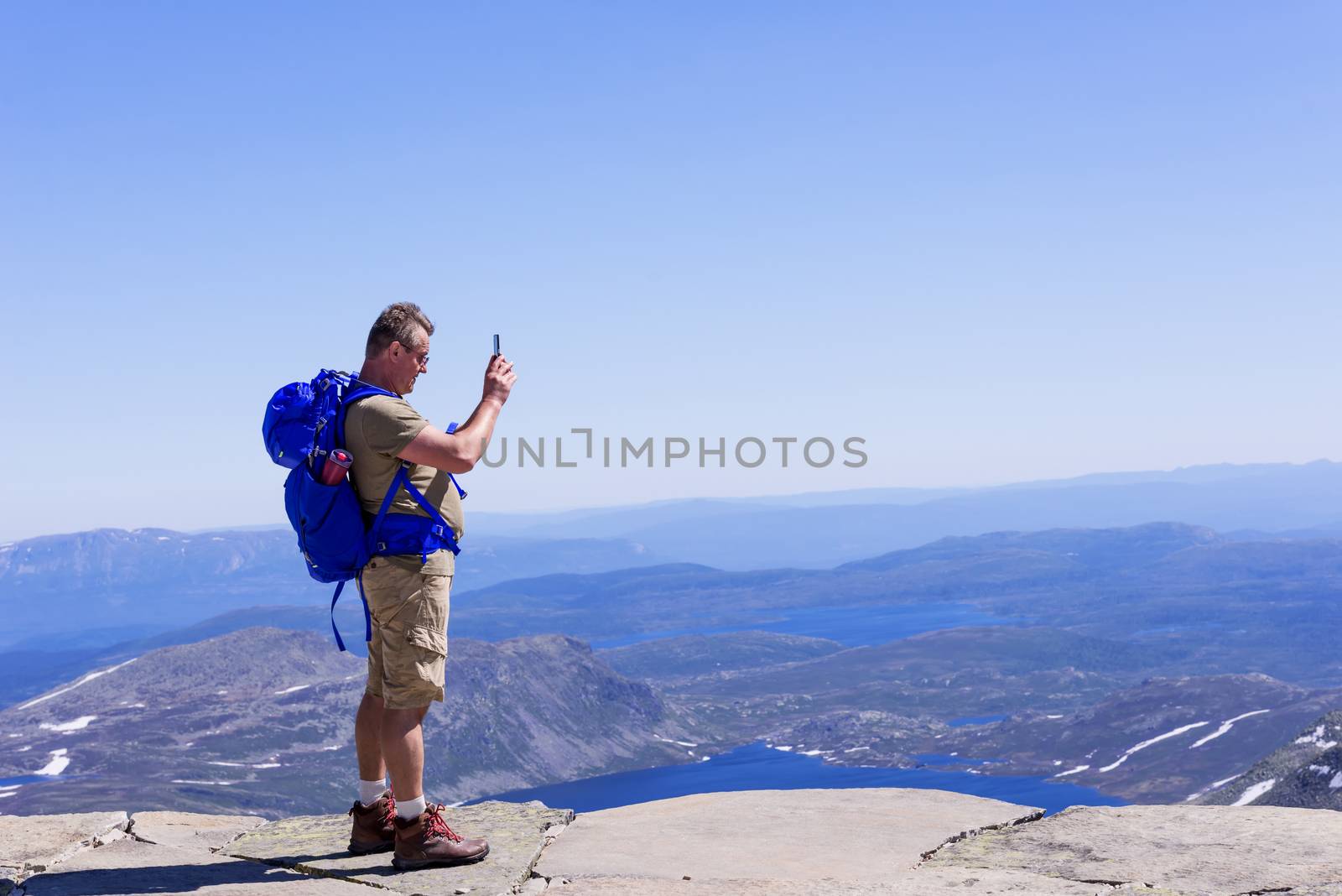 Hiker with big traveling rucksack taking pictures on the phone on the mountain trail, adventure travel and discovery