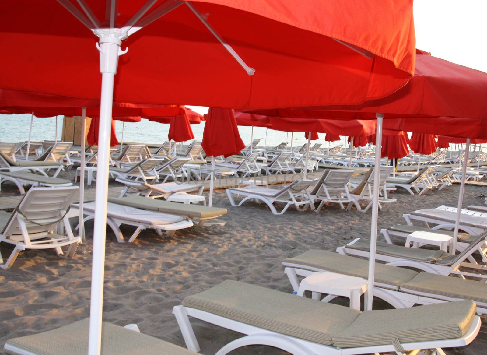 Plenty of sun loungers in a row on the coast. Folding chairs on the beach. Sandy beach, sunbeds with mattresses.  by alexx60