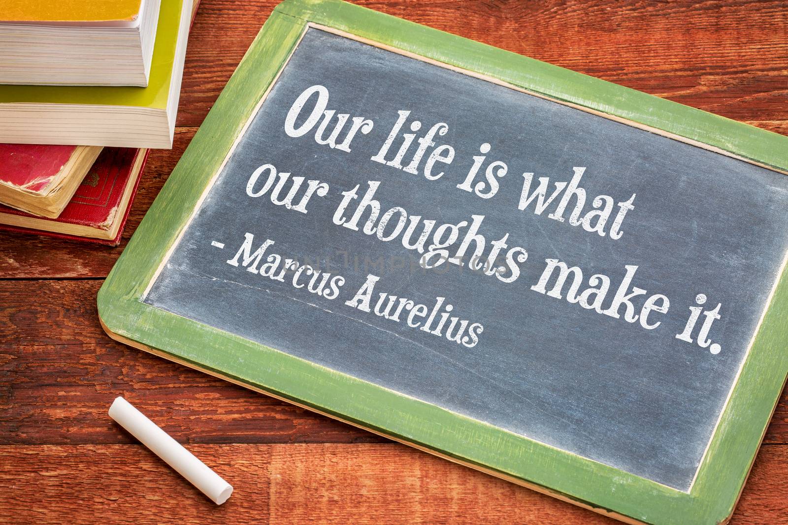 Our life is what our thoughts make it - inspirational word by Marcus Aurelius on a slate blackboard with a white chalk and a stack of books against rustic wooden table