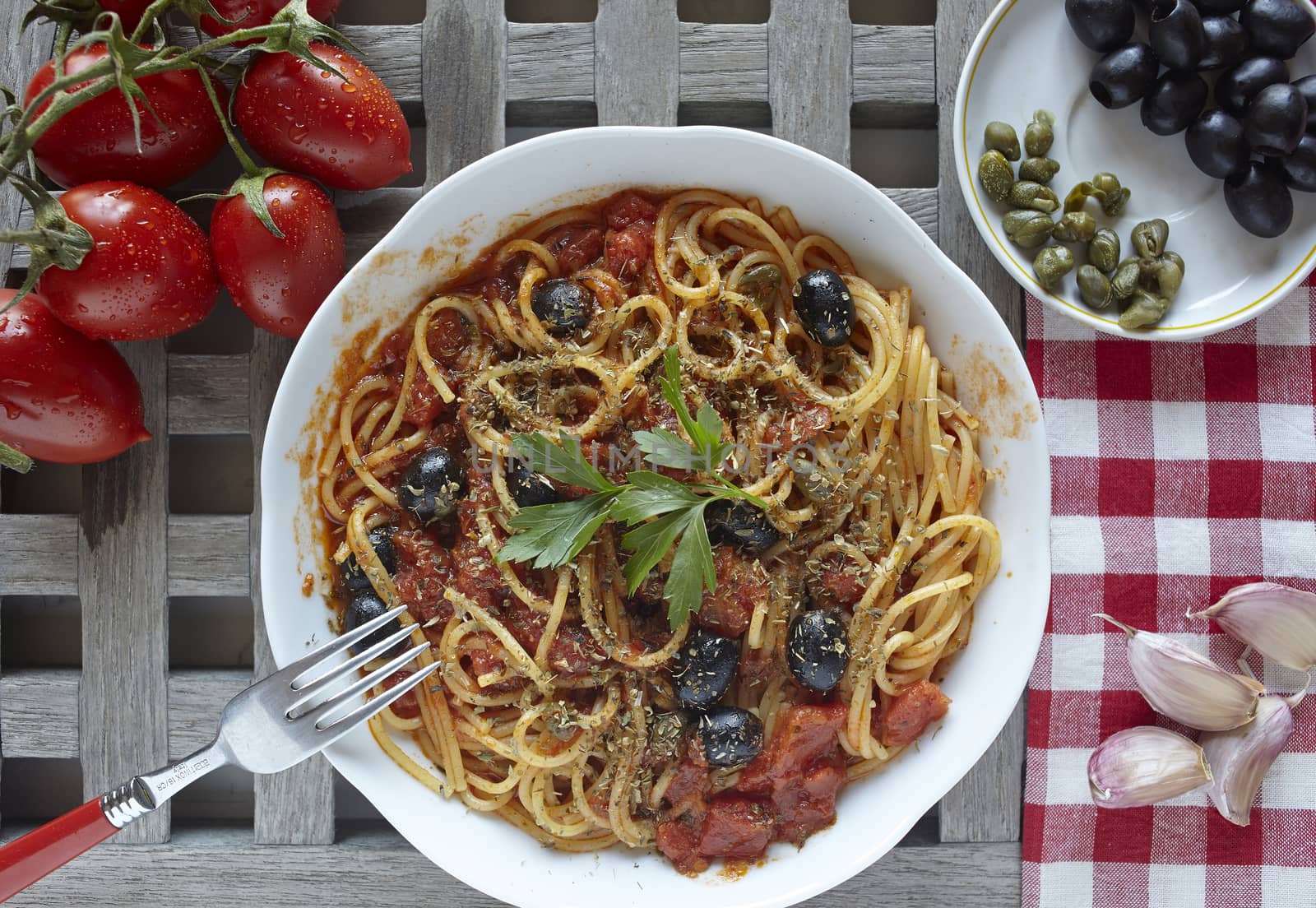 italian food: pasta with tomatoes, olives and capers, called put by belinchephoto