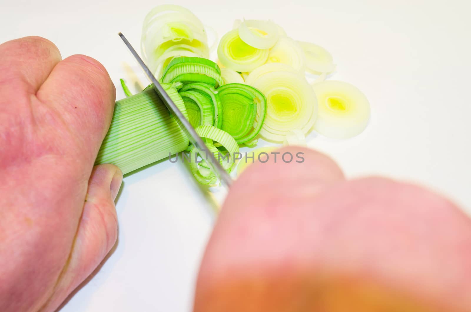 Hand of the cook, while cutting vegetables on a wooden board.