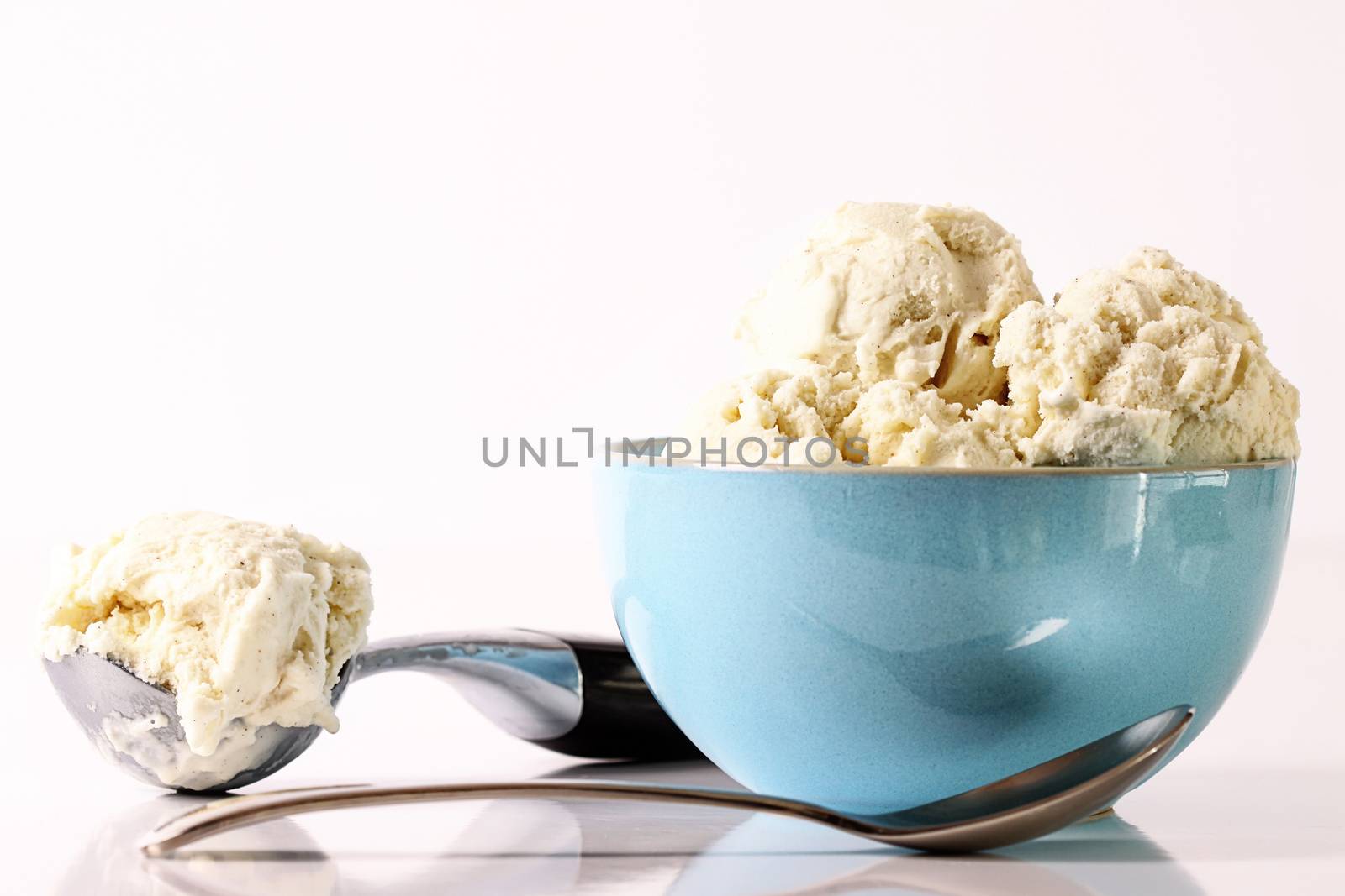 Vanilla ice cream in blue bowl with scooper and spoon