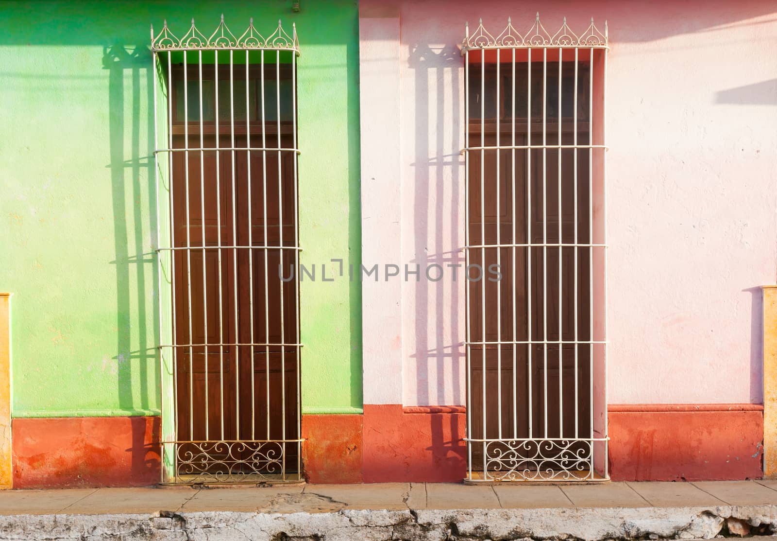 Barred doors two homes differentiated by color and broken pavement in third world town