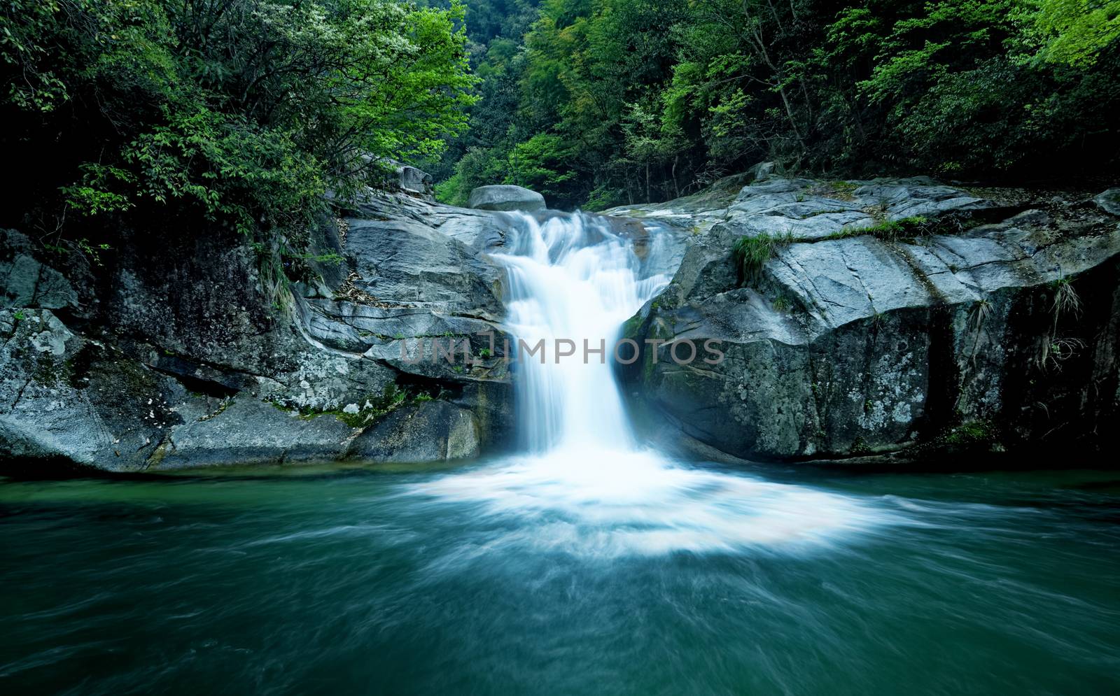 Large rain forest waterfall, sun beams, and mossy rocks