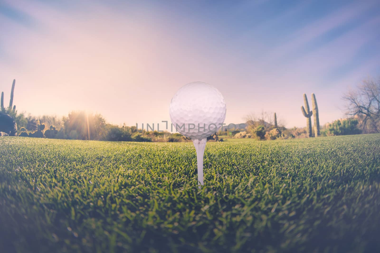 Super wide angle view of golf ball on tee with desert fairway and stunning Arizona sunset in background by Paulmatthewphoto