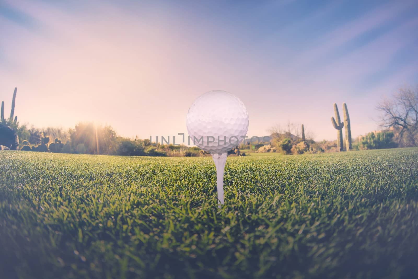 Super wide angle view of golf ball on tee with desert fairway and stunning Arizona sunset in background