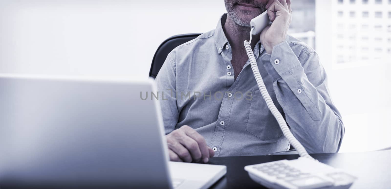 Businessman on call in front of laptop at office desk by Wavebreakmedia