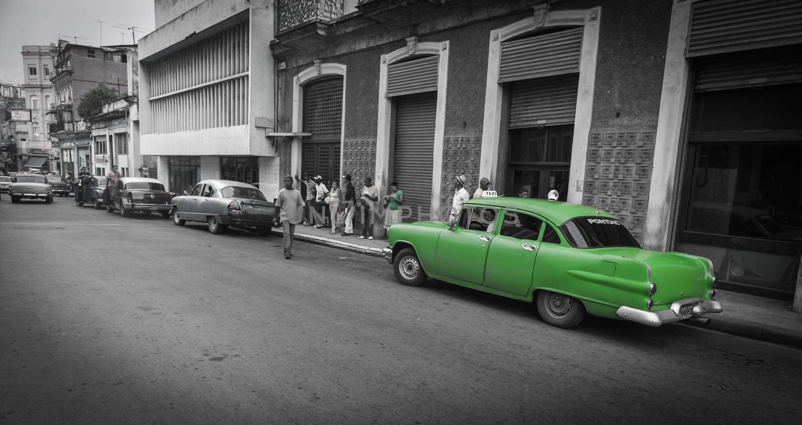 Havana street scene in monochrome old dilapidated buildings, people walking and bright green American classic Pontiac car.