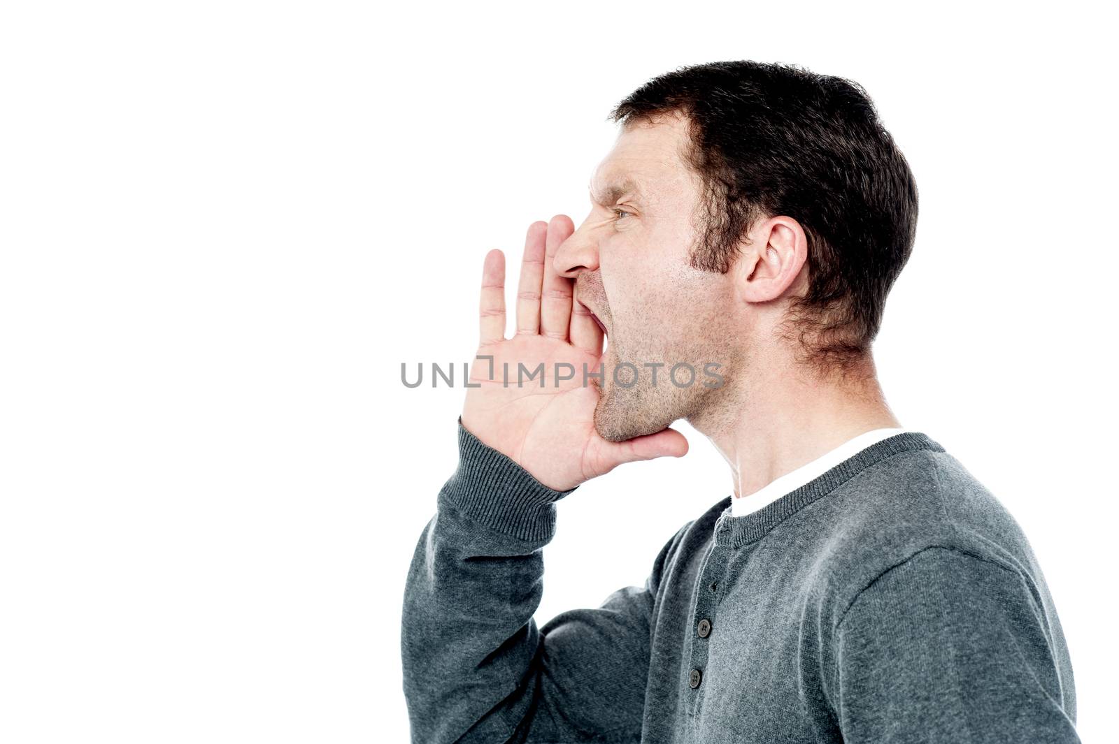 Side pose of man shouting, hands near his mouth.