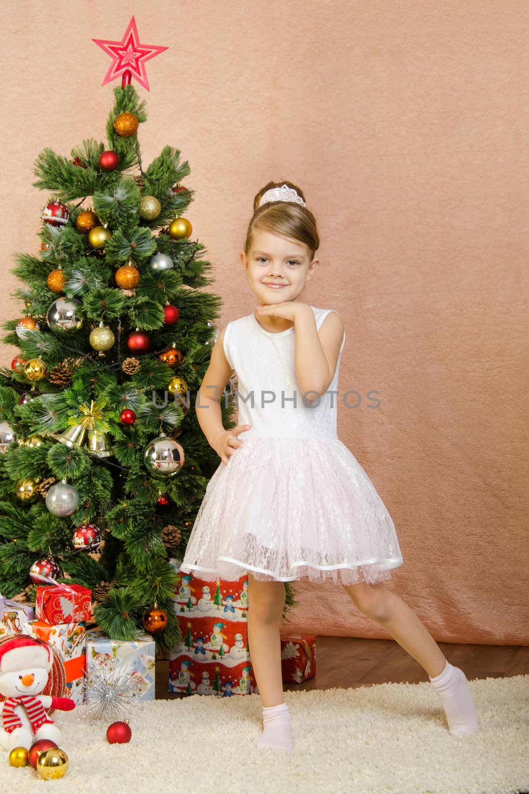 Five-year girl in a New Year's dress standing on a mat at the Christmas tree