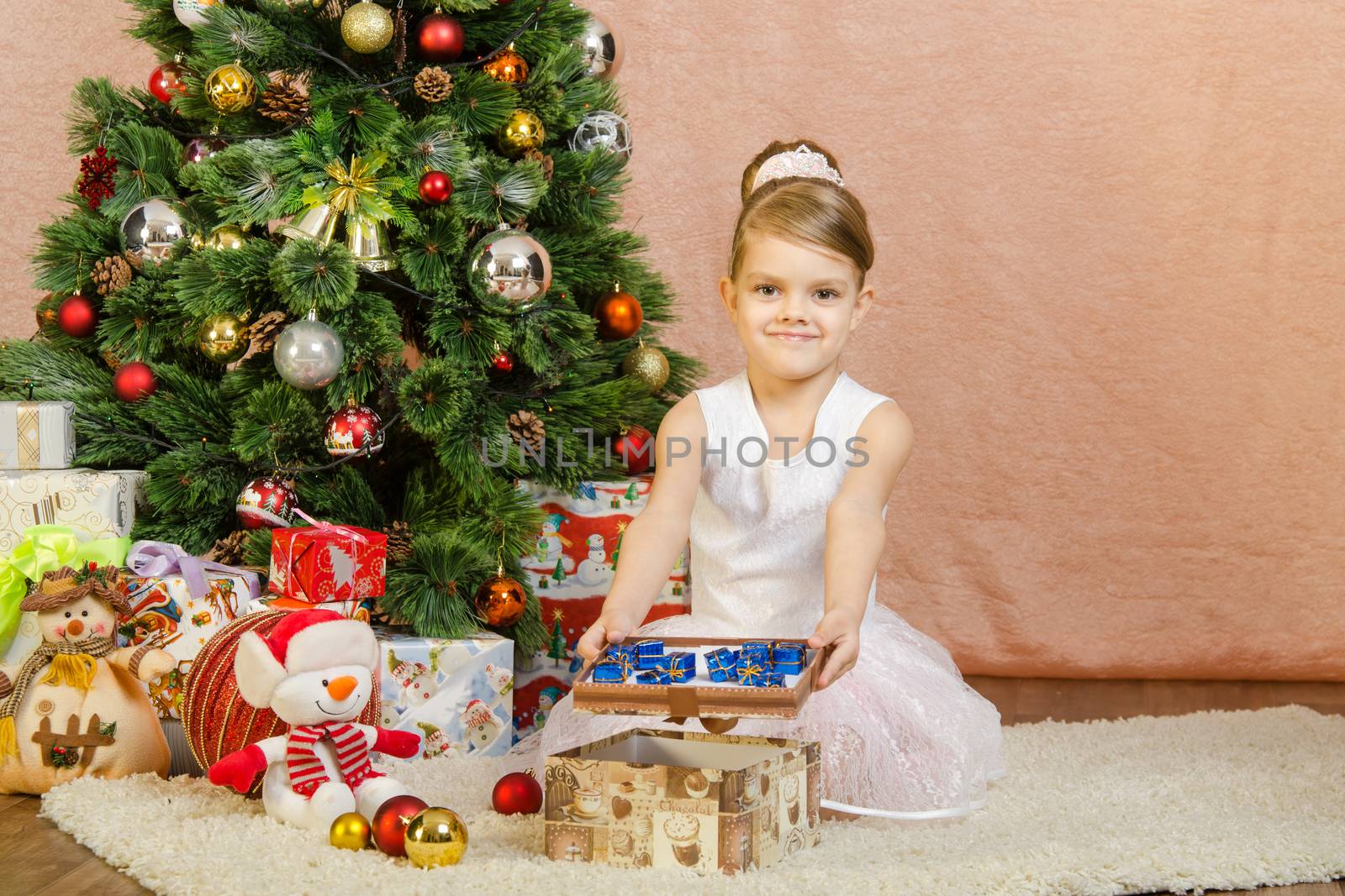 Five-year girl in a New Year's dress sitting on a mat at the Christmas tree