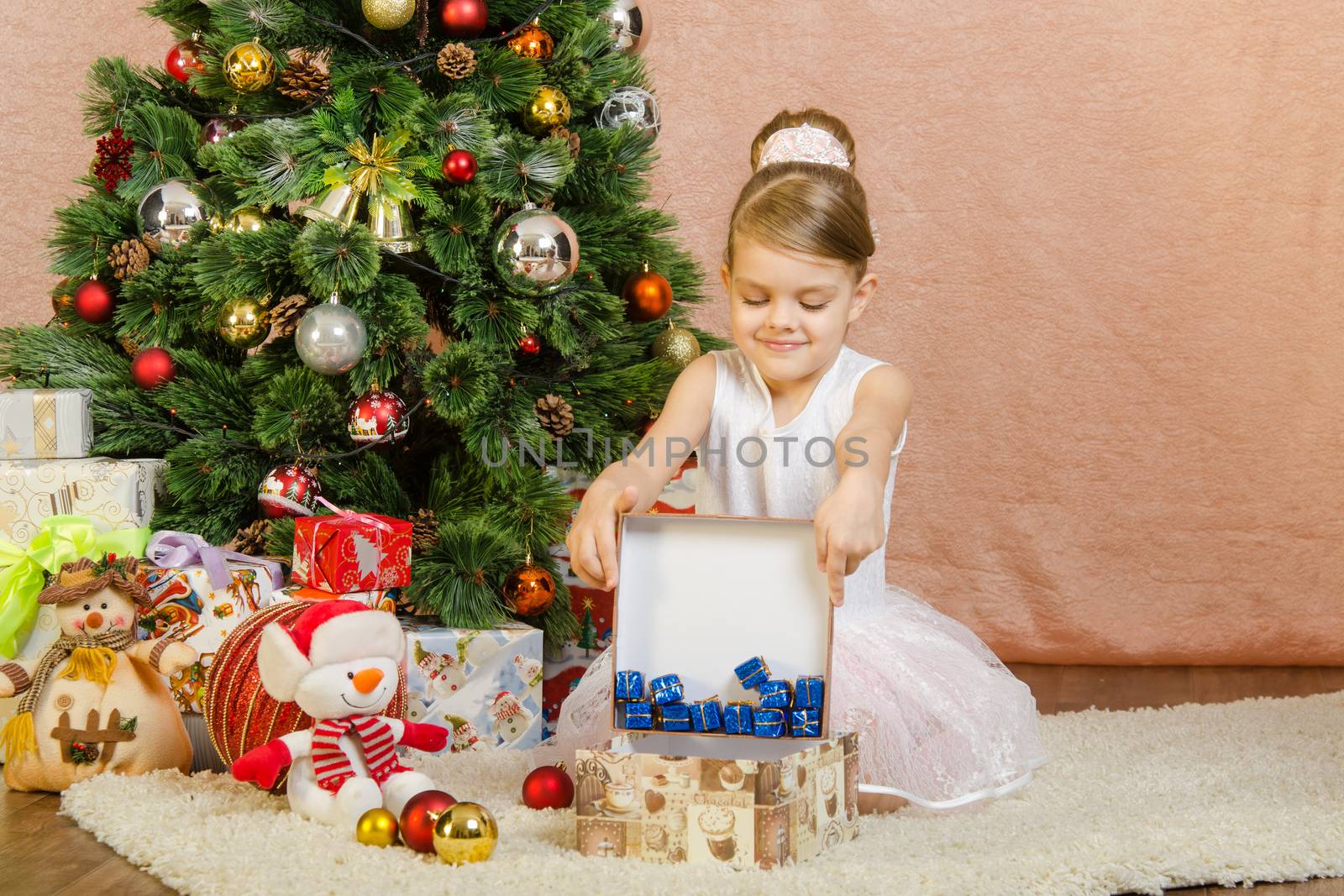 Five-year girl in a New Year's dress sitting on a mat at the Christmas tree