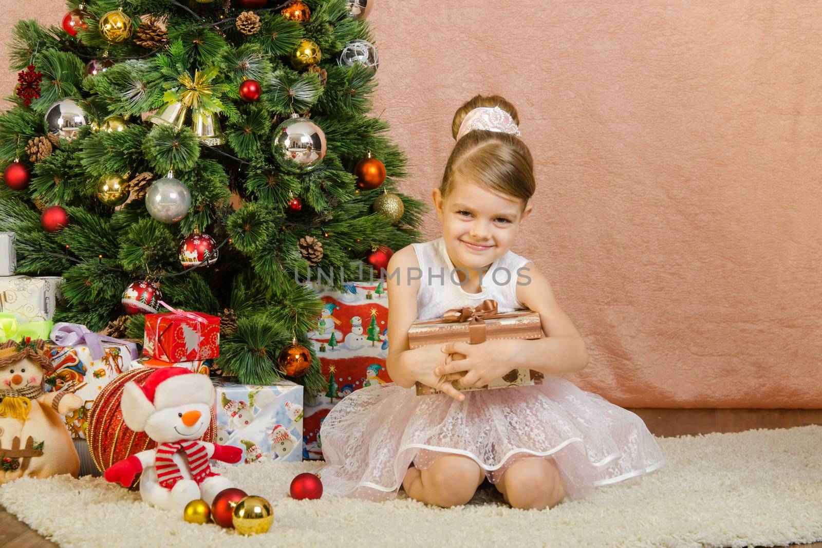 Five-year girl in a New Year's dress sitting on a mat at the Christmas tree