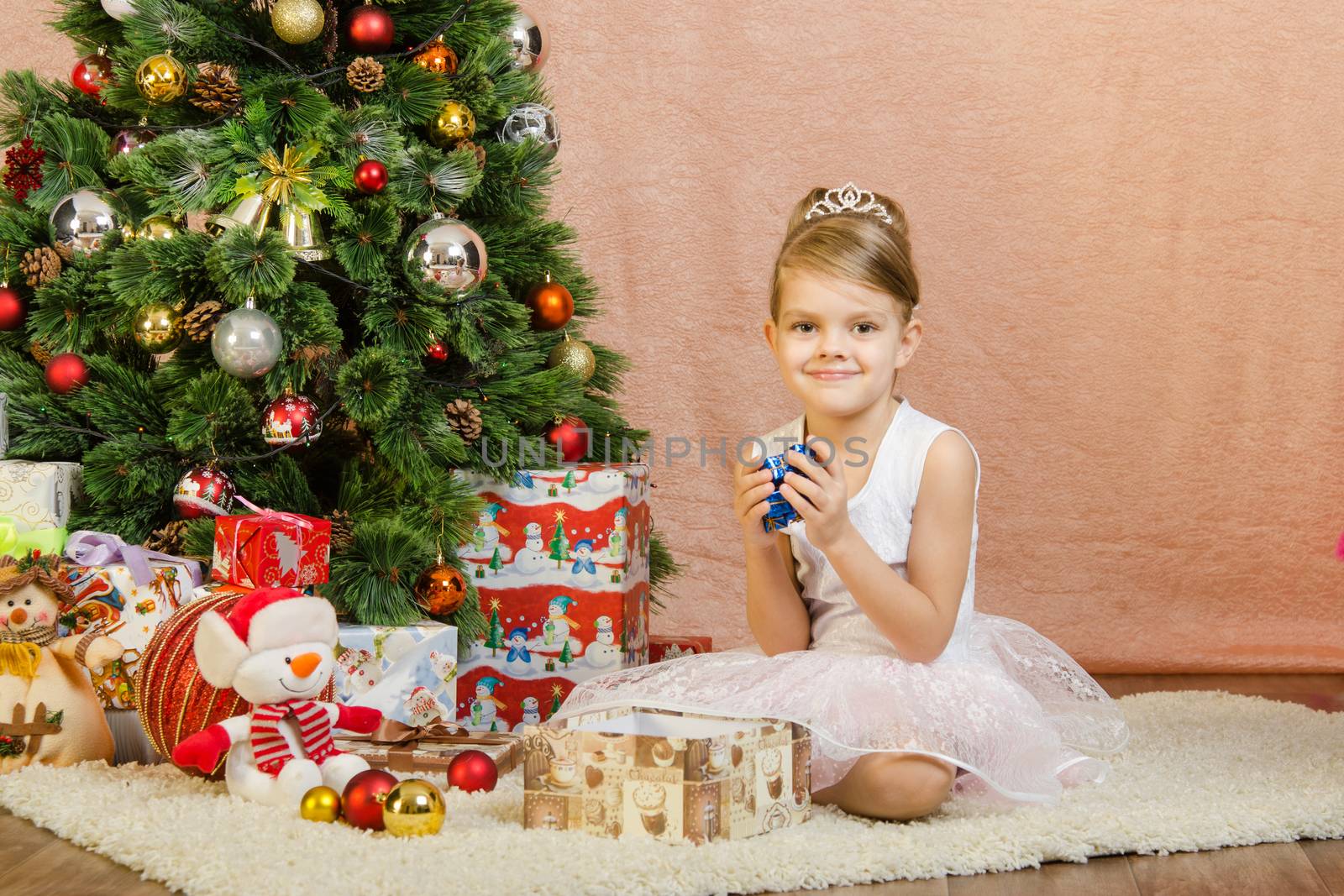 Five-year girl in a New Year's dress sitting on a mat at the Christmas tree