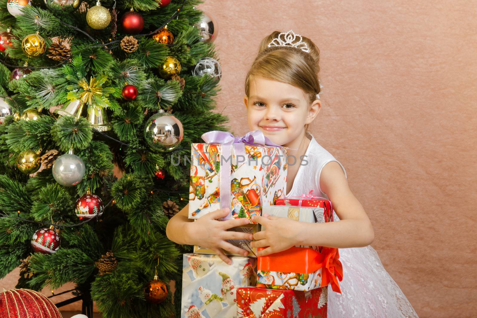 Five-year girl in a New Year's dress sitting on a mat at the Christmas tree
