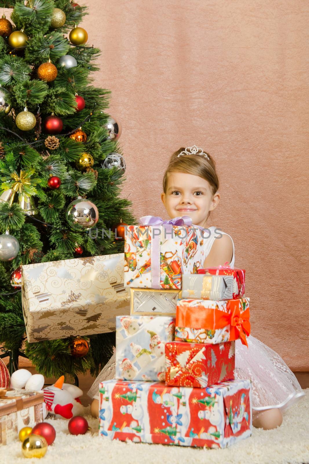 Five-year girl in a New Year's dress sitting on a mat at the Christmas tree