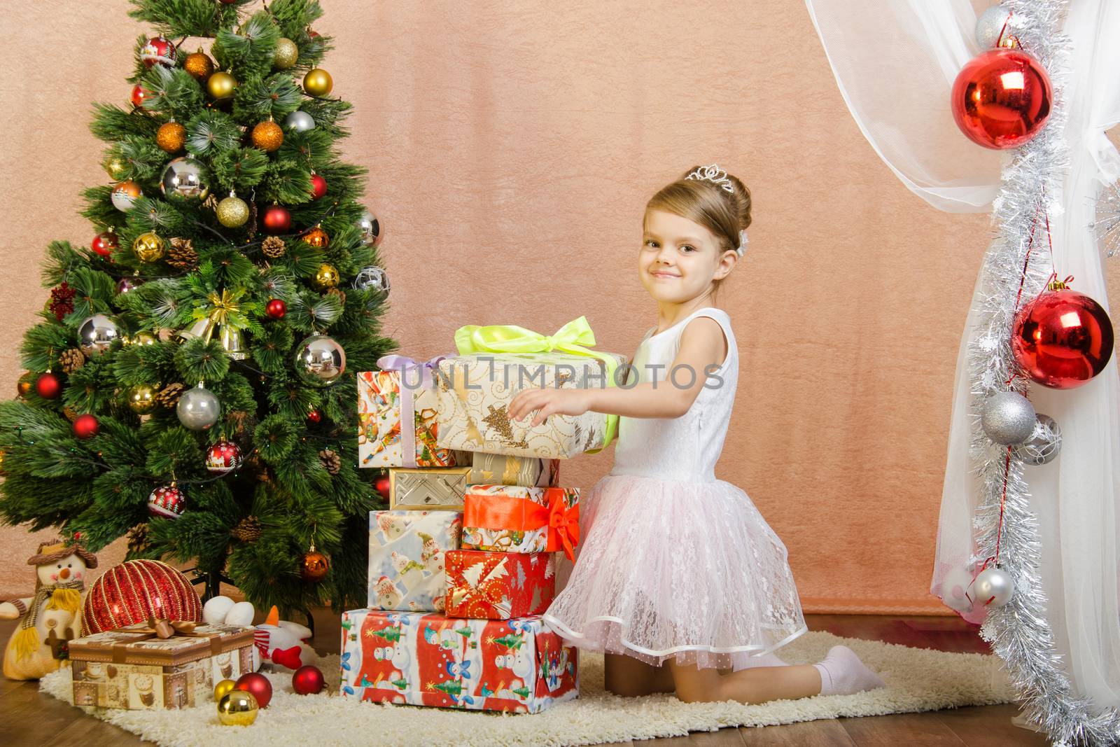 Five-year girl in a New Year's dress sitting on a mat at the Christmas tree
