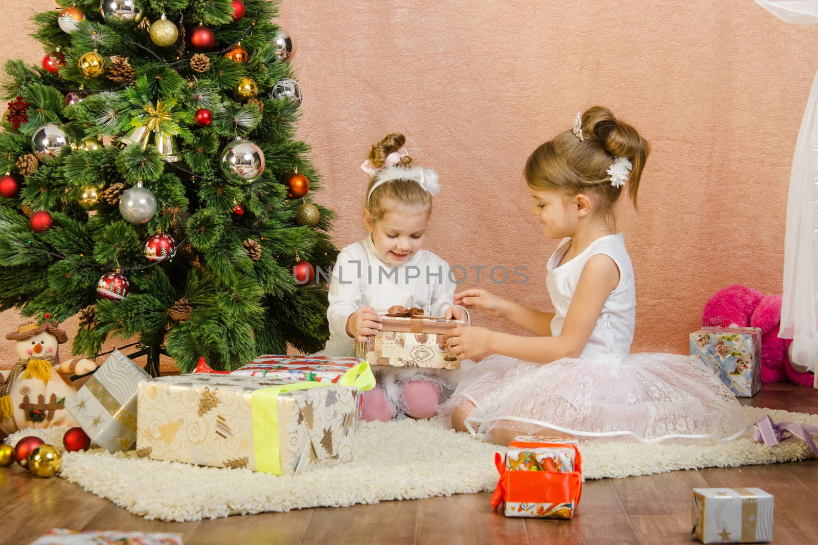 Five-year and three-year girl in a New Year's dress sitting on a mat at the Christmas tree