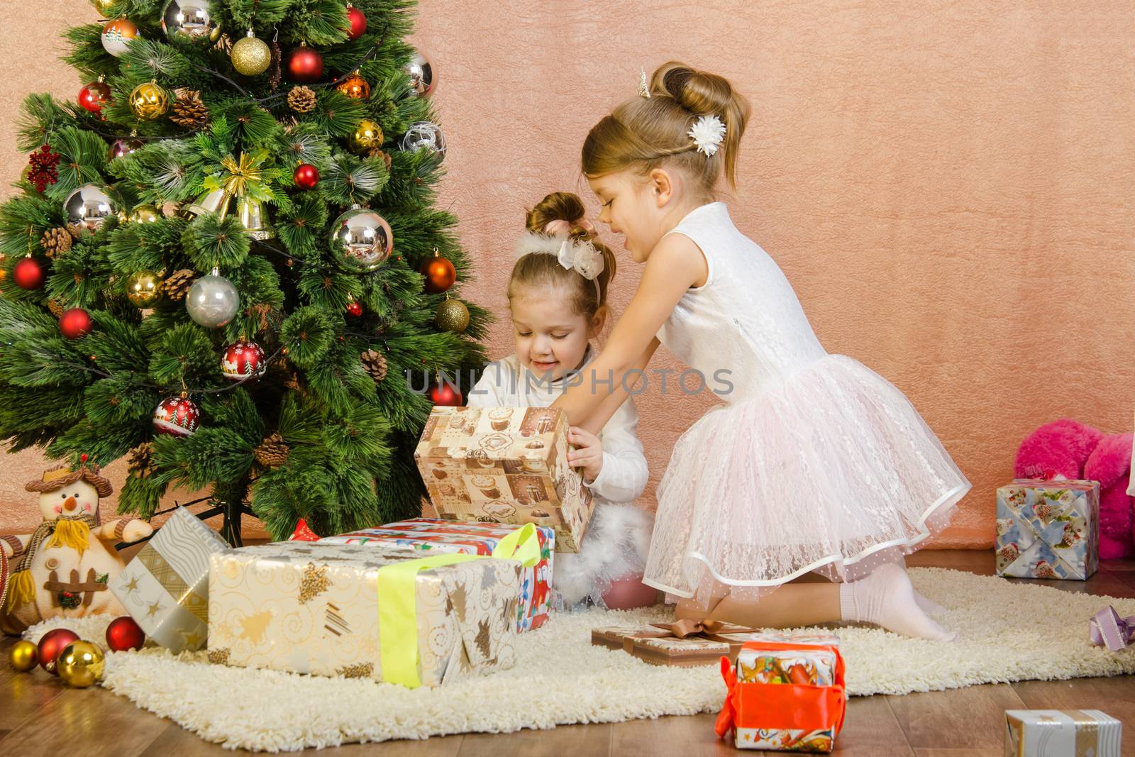 Five-year and three-year girl in a New Year's dress sitting on a mat at the Christmas tree