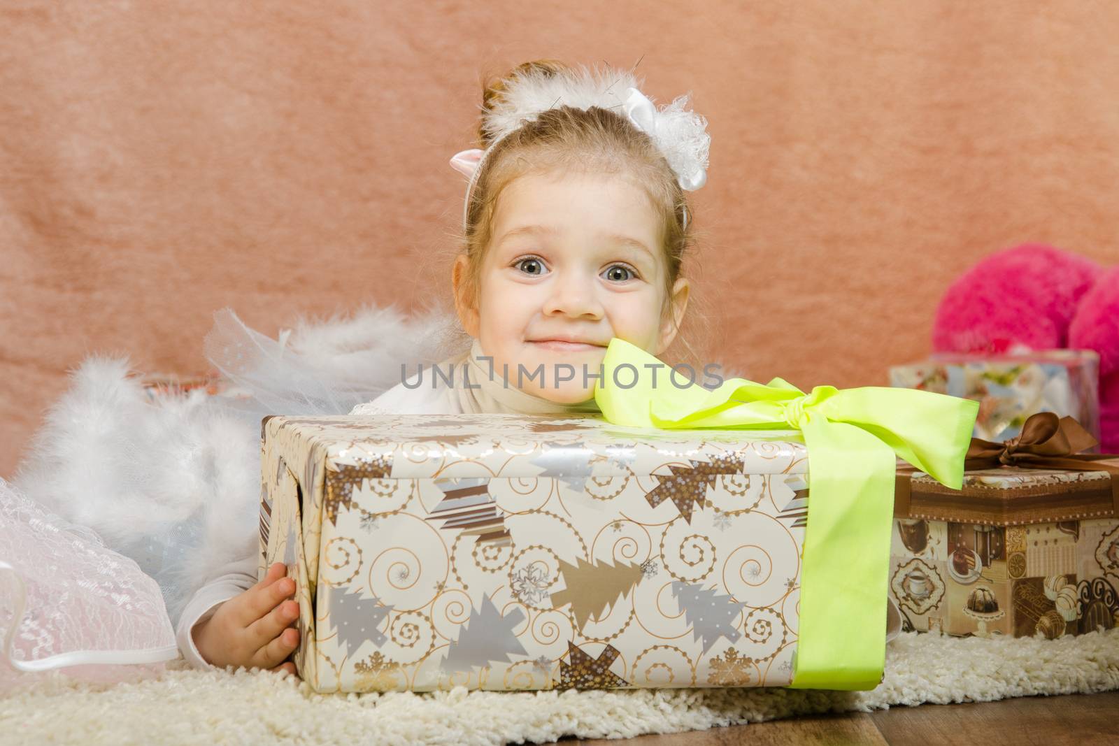 The three-year girl in a New Year's dress sitting on a mat at the Christmas tree