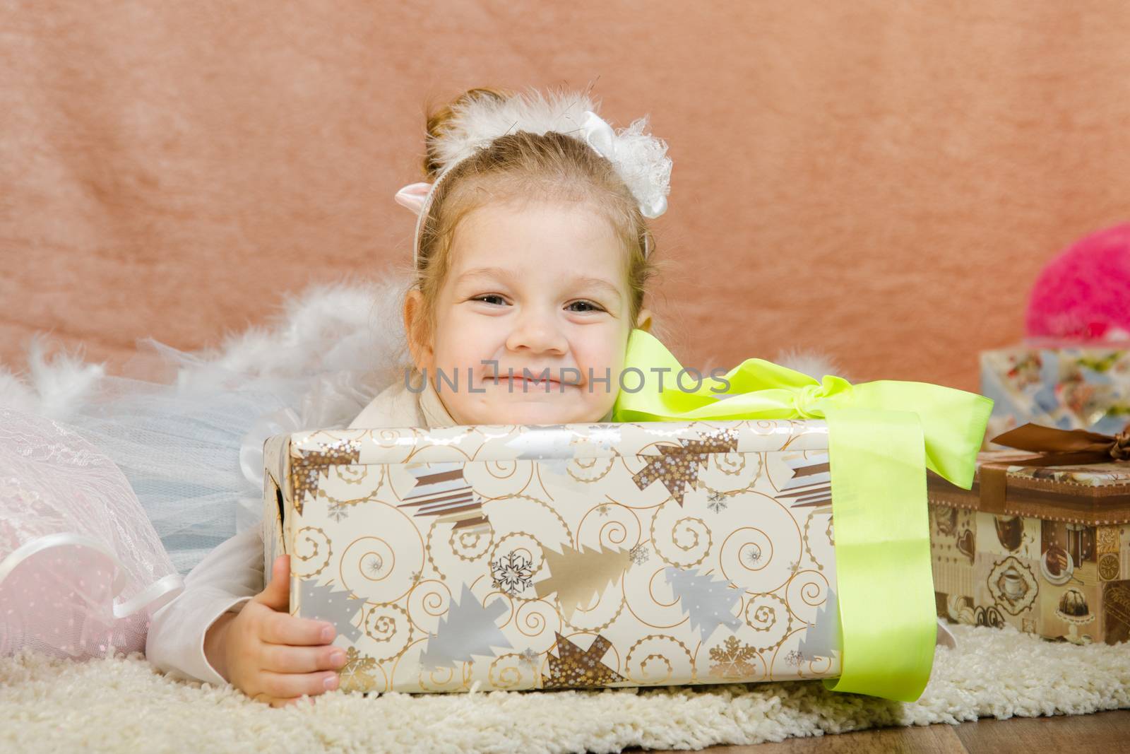 The three-year girl in a New Year's dress sitting on a mat at the Christmas tree