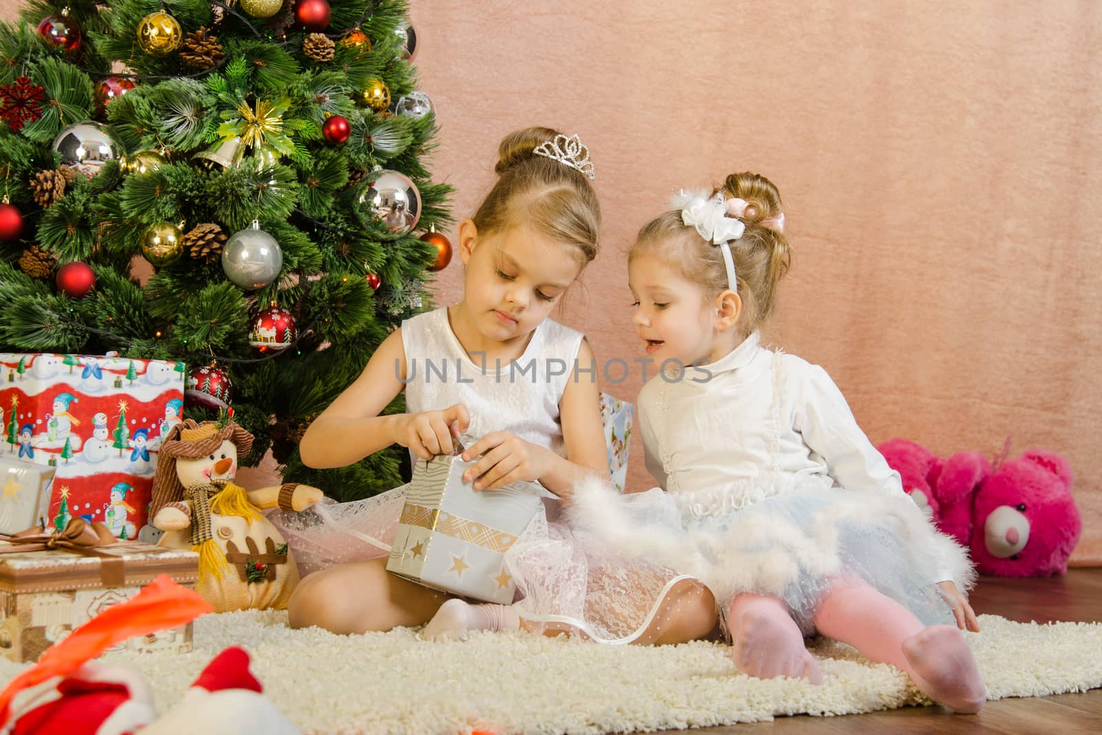 Five-year and three-year girl in a New Year's dress sitting on a mat at the Christmas tree