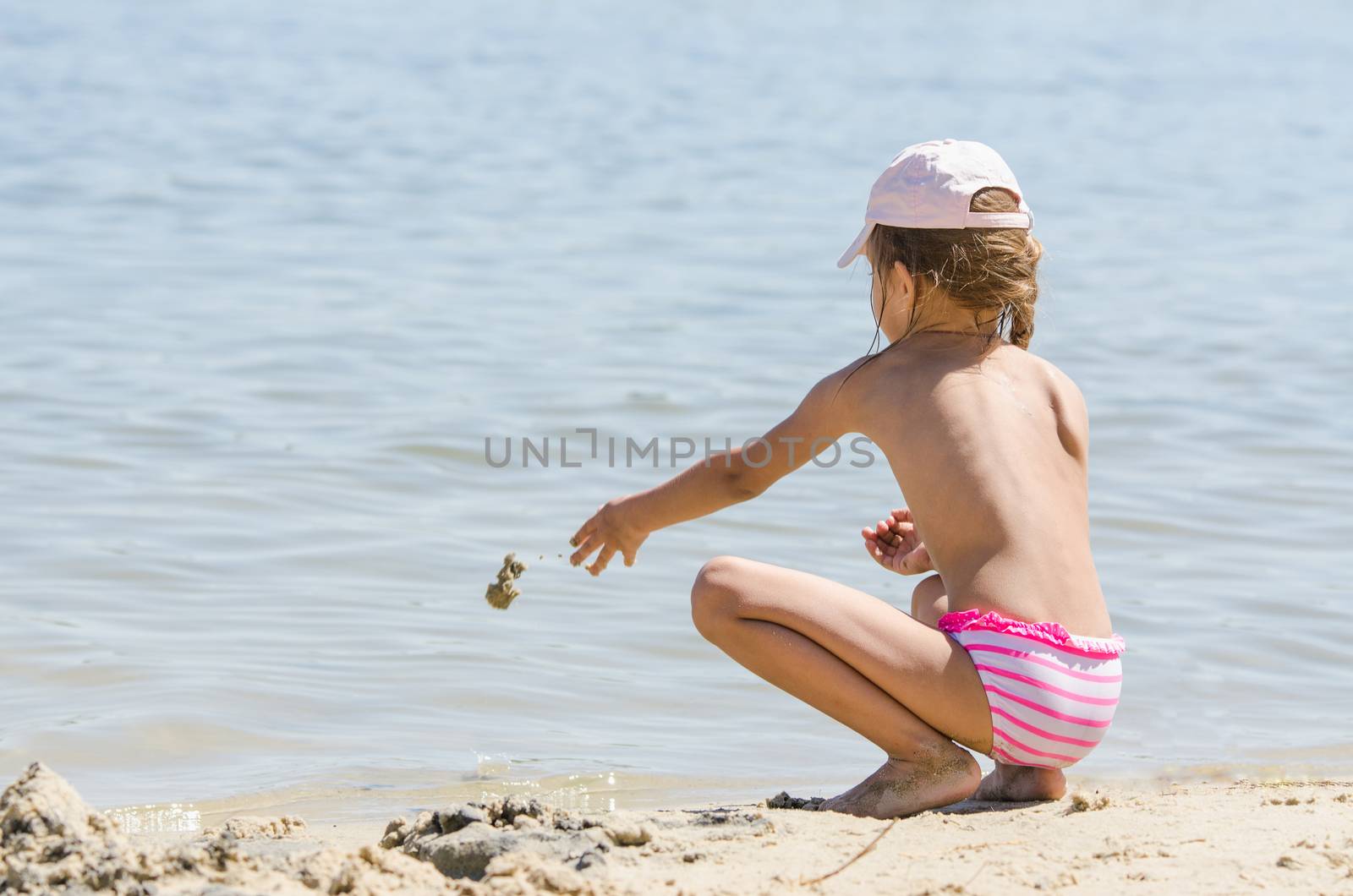 Girl sitting on the river bank and throwing sand in the water