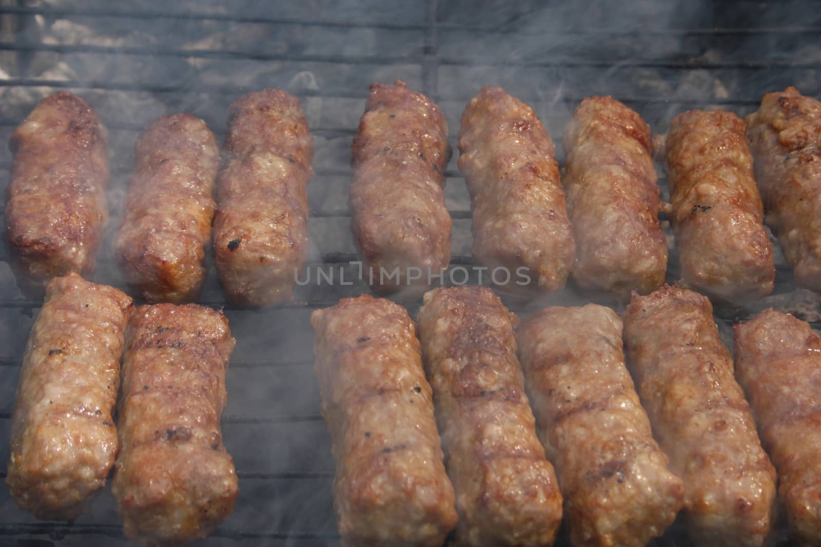 Barbecuing minced meat, traditional Romanian preparation for barbecue, called "mici",  on charcoal fire - closeup image.
