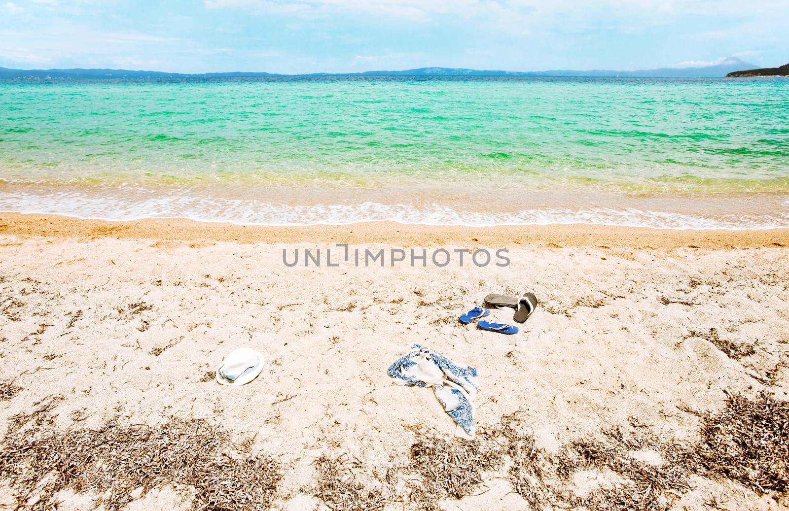 Beautiful seascape with clear calm green water. No body on it, just two pairs of sandals, a hat and a scarf.